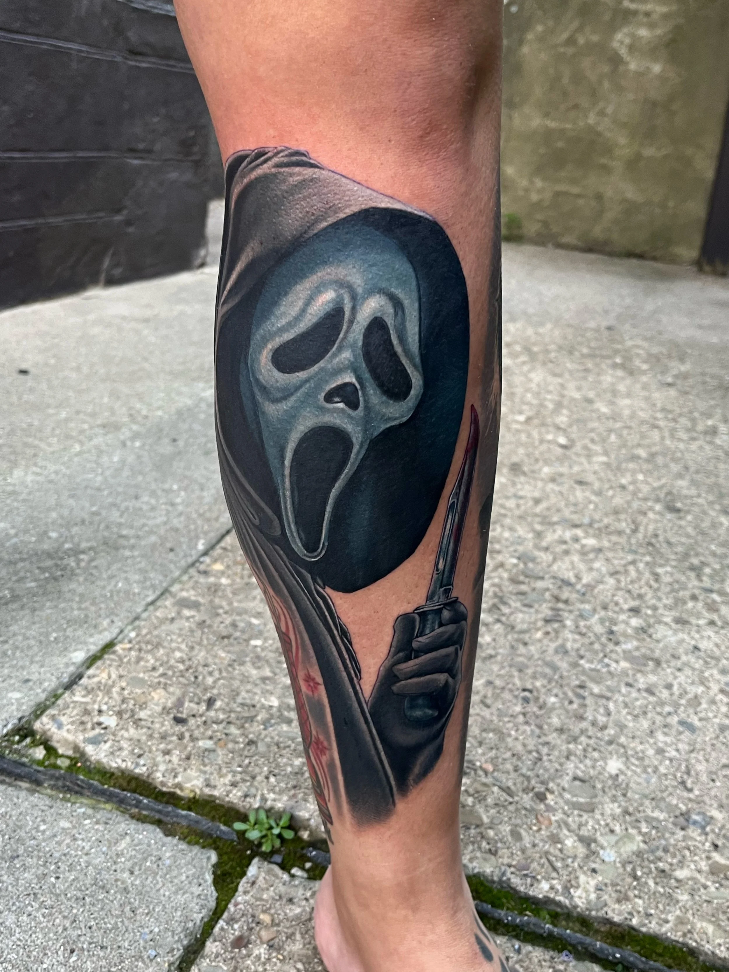 Close-up of a person's calf featuring a tattoo of a ghost face mask from the Scream movie by Jesse Smith tattoo artist in Bethel Park, PA.