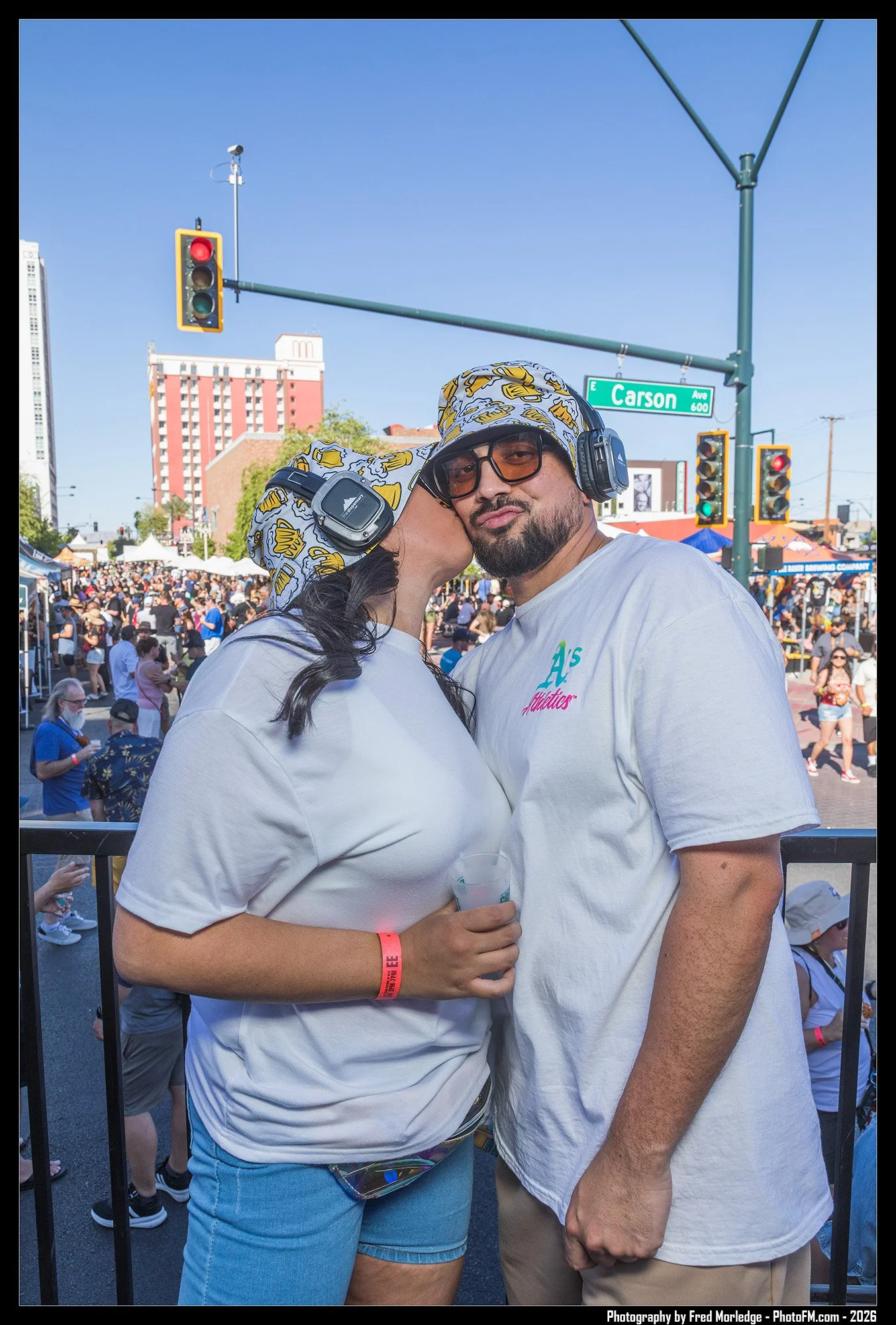 Two people embracing at an outdoor event during the daytime, with a crowd in the background and traffic lights overhead.