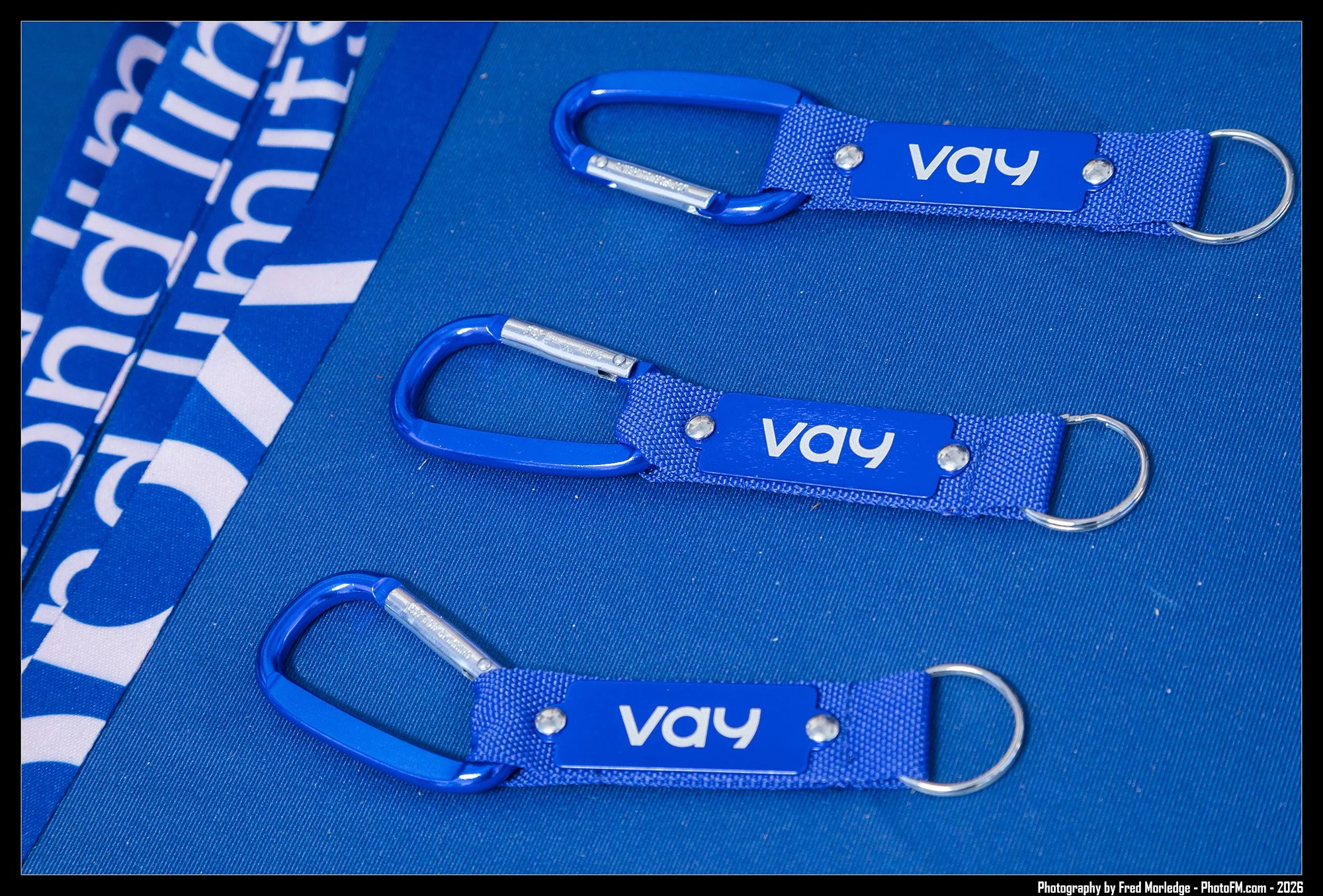 Blue fabric lanyards with silver clips and the word "Vay" printed on them, arranged on a blue surface with partial blue and white branding.