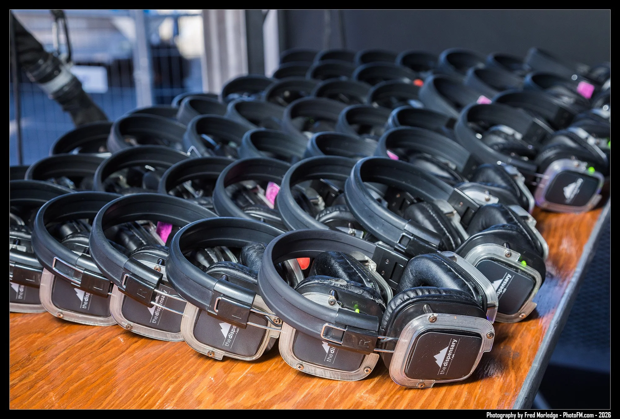 Multiple black wireless headphones arranged in rows on a wooden surface.