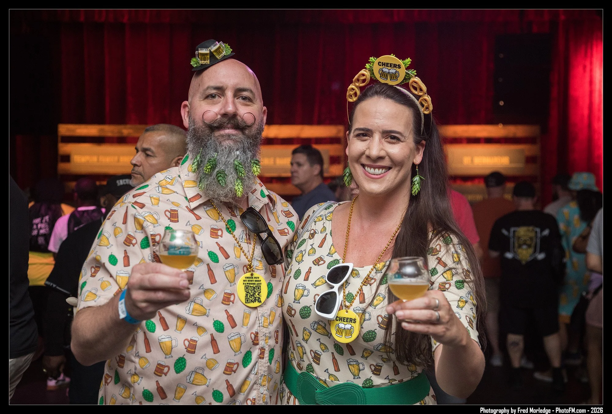 A man and woman celebrating at a party, both wearing beer-themed outfits and headbands with beer-related decorations, holding glasses of beer and smiling.