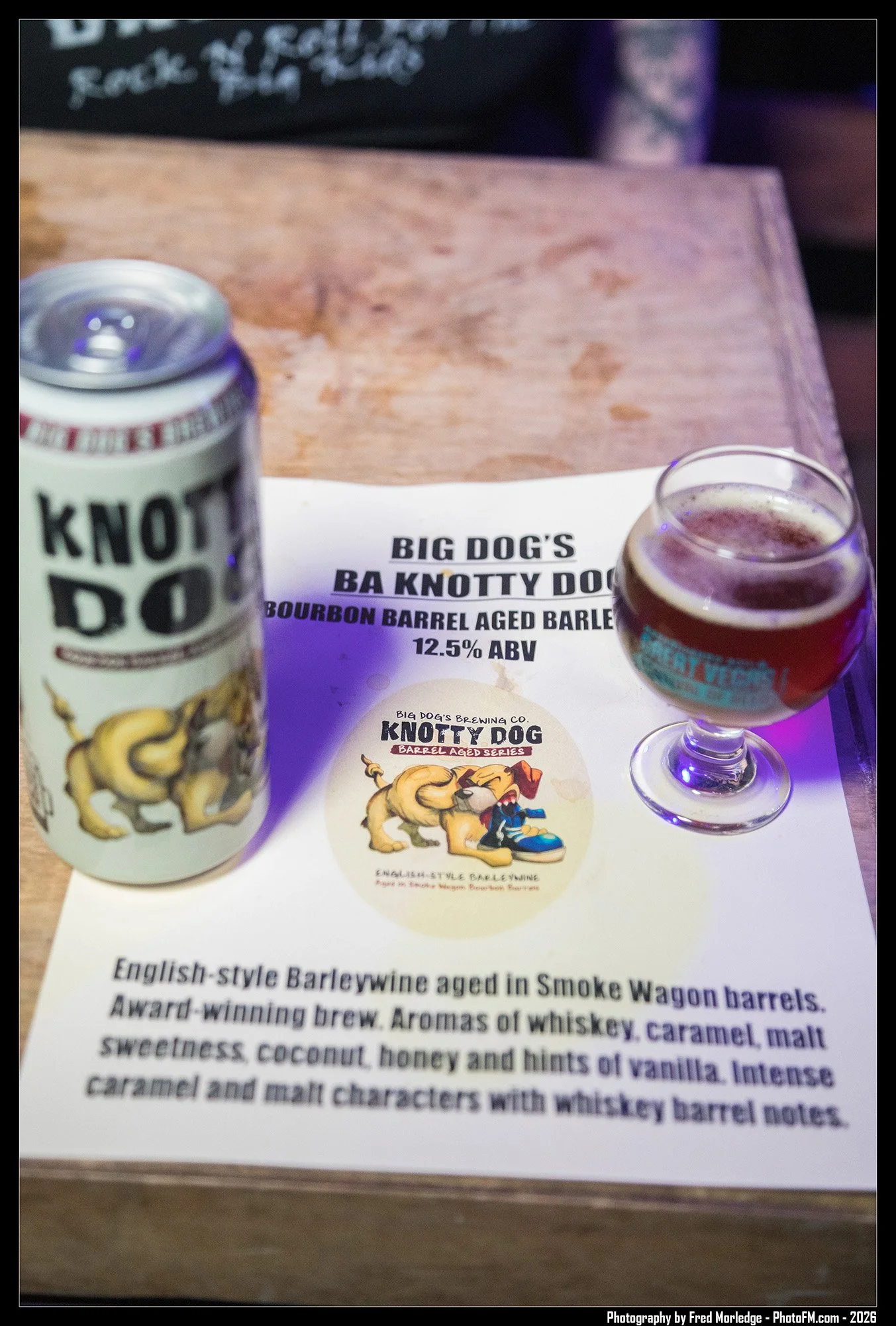 A menu page for Big Dog's Barrel Aged Series beer, specifically English-style barleywine aged in Smoke Wagon barrels, with 12.5% ABV. The page features a can of Knot Dog beer with a cartoon illustration of a dog and a glass of beer on a wooden table,