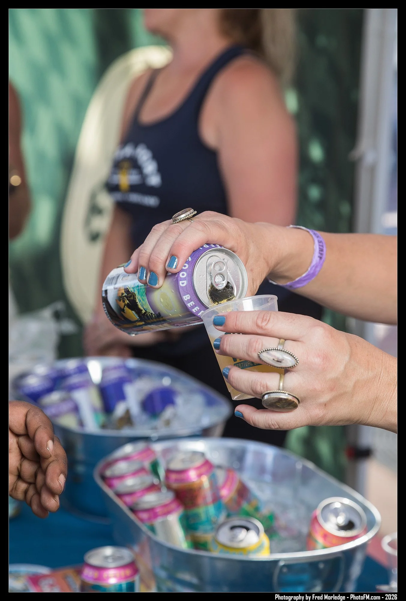 A person pouring a canned beverage into a plastic cup at a gathering, with a bowl of canned drinks in the background.