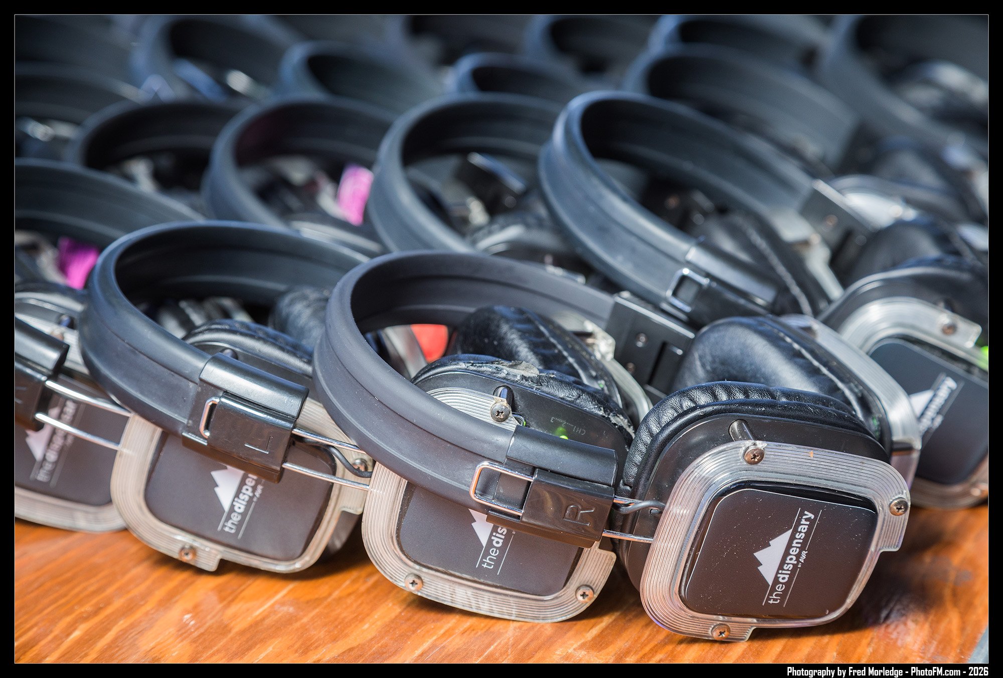A collection of black and gray over-ear headphones with labels, placed on a wooden surface.
