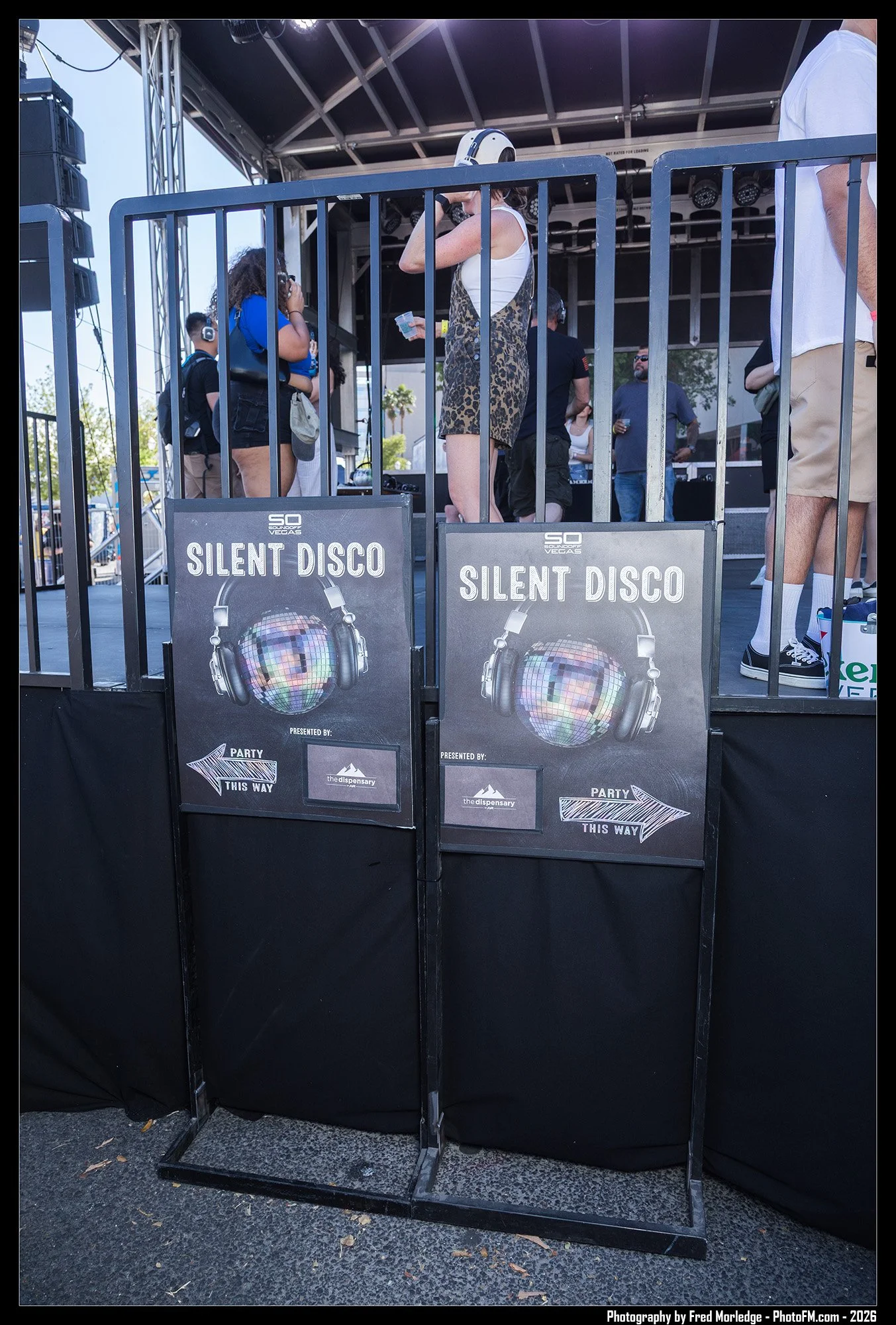 People gathered at a stage with signs reading 'Silent Disco' and a large headphoned illustration, indicating a silent dance event.
