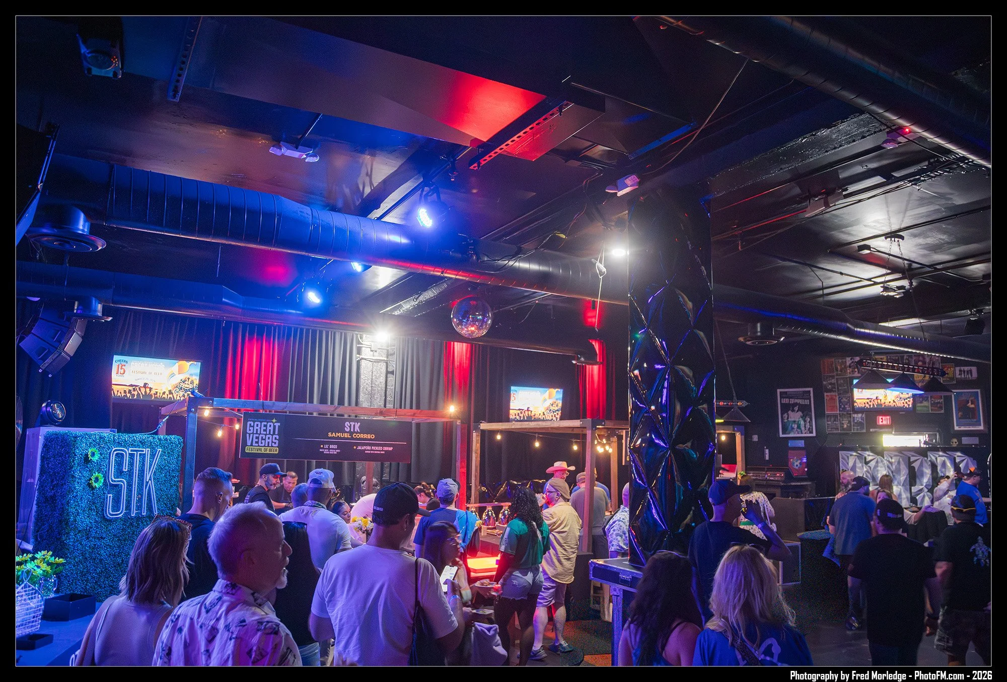 Crowd of people at the Great Vegas Festival of Beer inside a dimly lit venue with colorful lights, a bar area, and signage with event details.