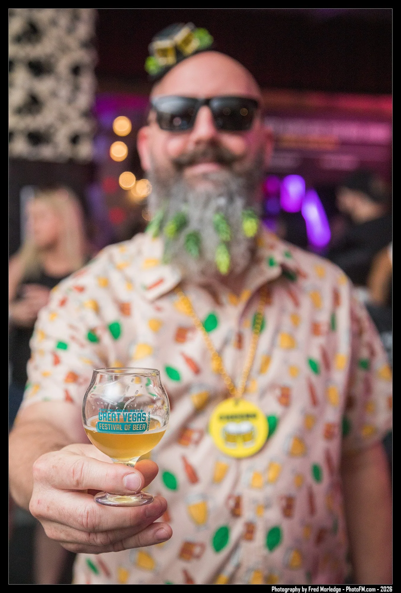 A man with a gray beard wearing sunglasses and a colorful Hawaiian shirt holding a glass of beer at the Great Vegas Festival of Beer event.
