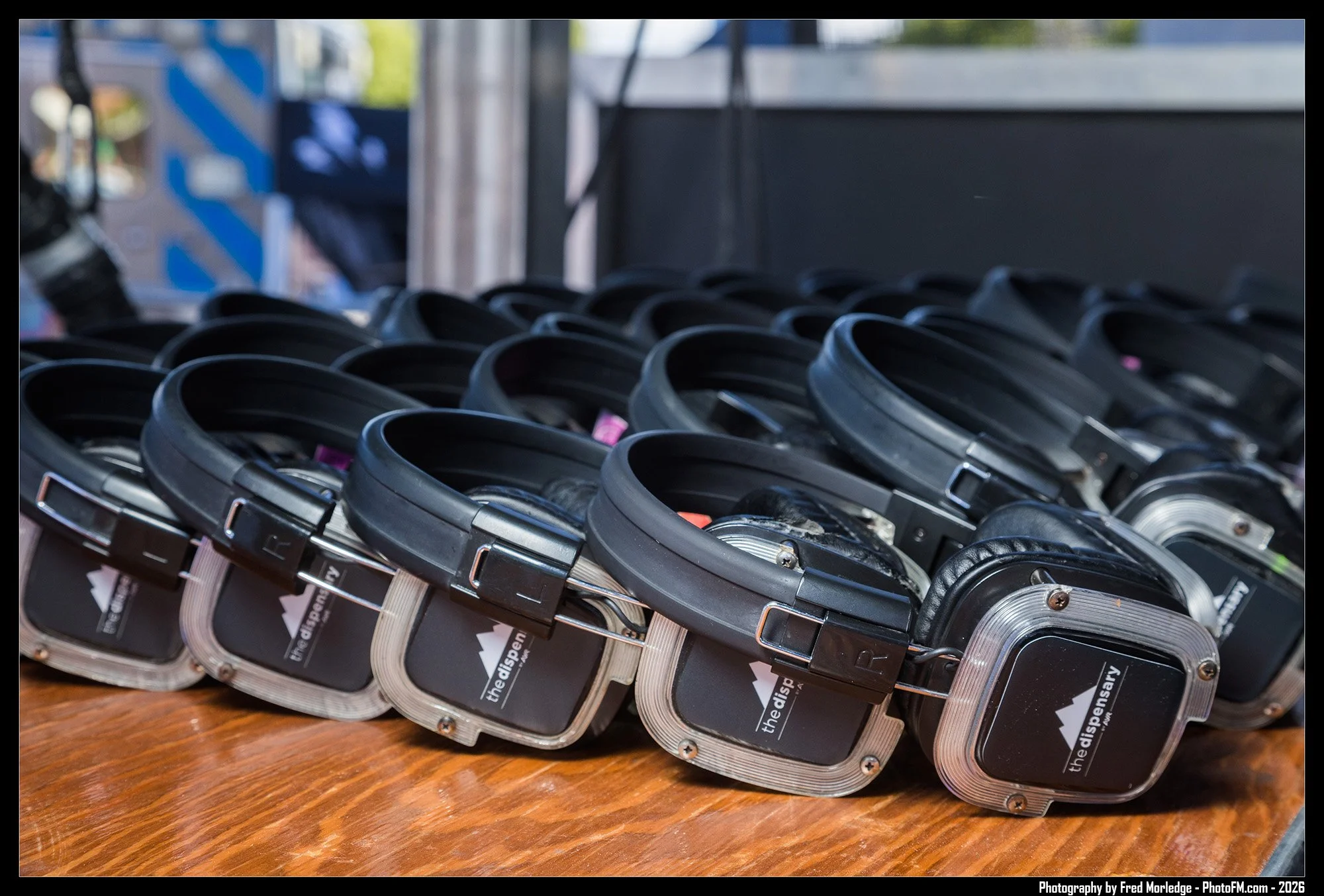 Multiple black and silver wireless headphones lined up on a wooden surface, with a blurred background.