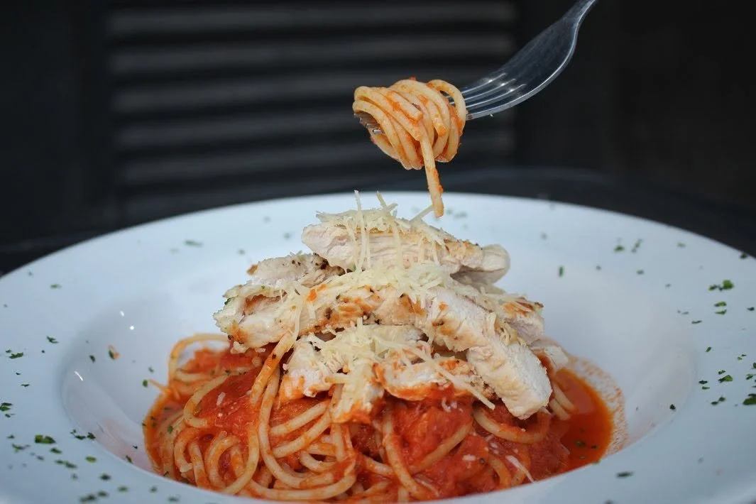Plato de pasta con salsa de tomate, pollo desmenuzado y queso rallado.