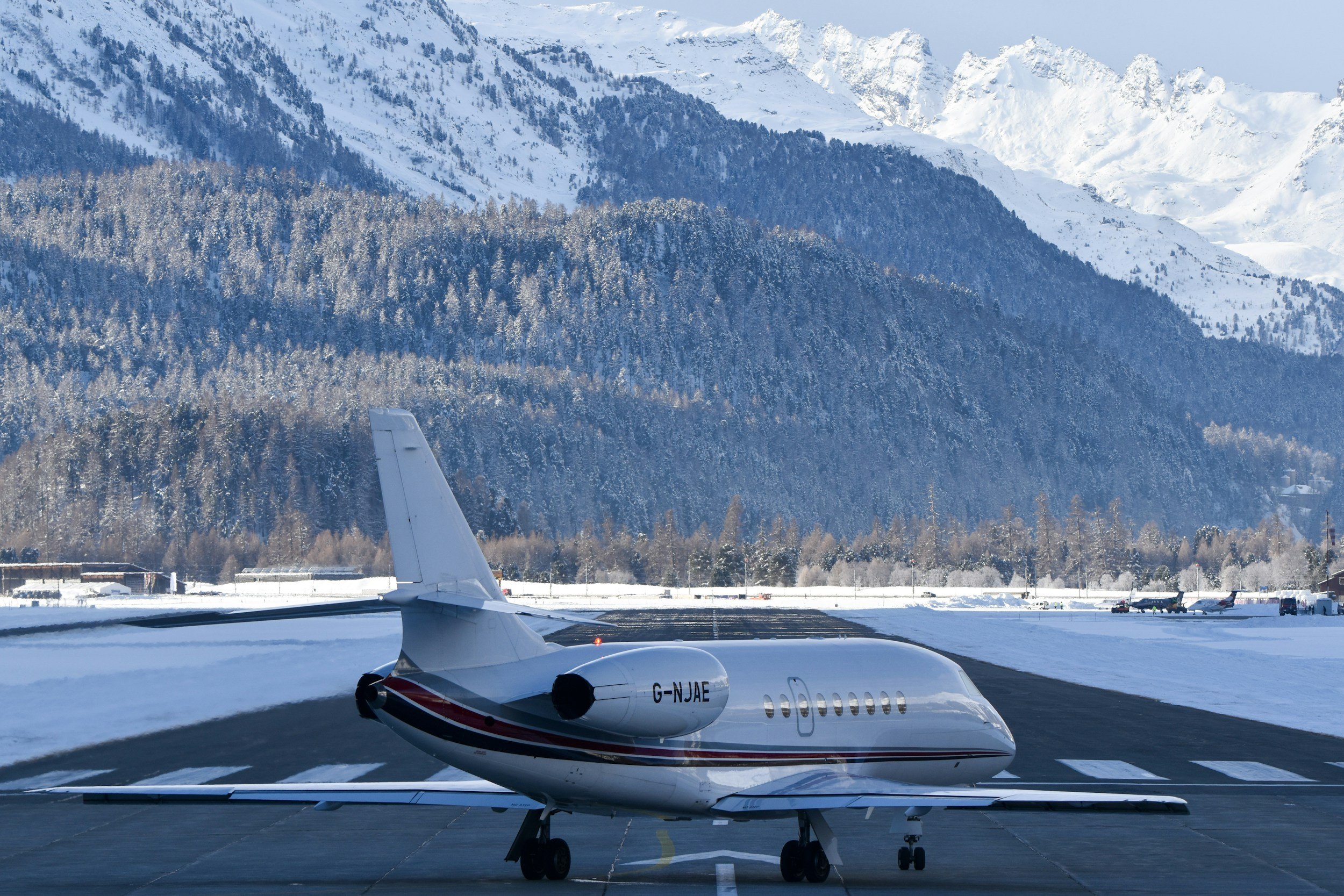 Small private jet on snow-covered runway at an airport surrounded by snow-capped mountains.