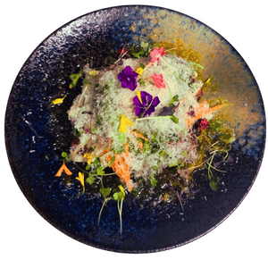 A breaded cutlet topped with shaved cheese, greens and edible flowers on a dark blue plate.
