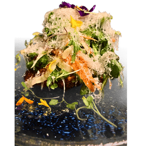 A tall mound of crisp greens and shaved vegetables plated on dark stone.