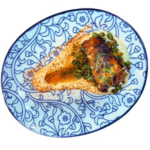 A fillet of fish topped with herbs and greens on a blue and white patterned plate.