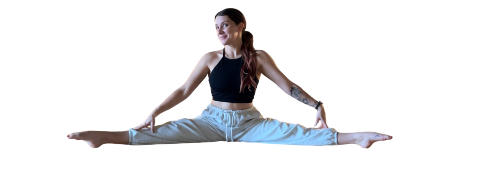 Young woman with long brown hair practicing splits yoga pose, wearing black sports bra and gray sweatpants.