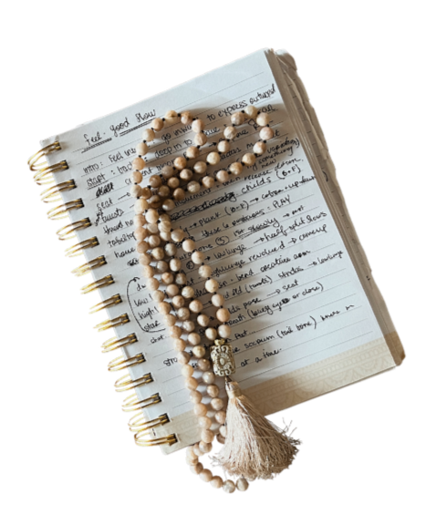 Open spiral notebook with handwritten notes and a tan beaded prayer rosary resting on top.