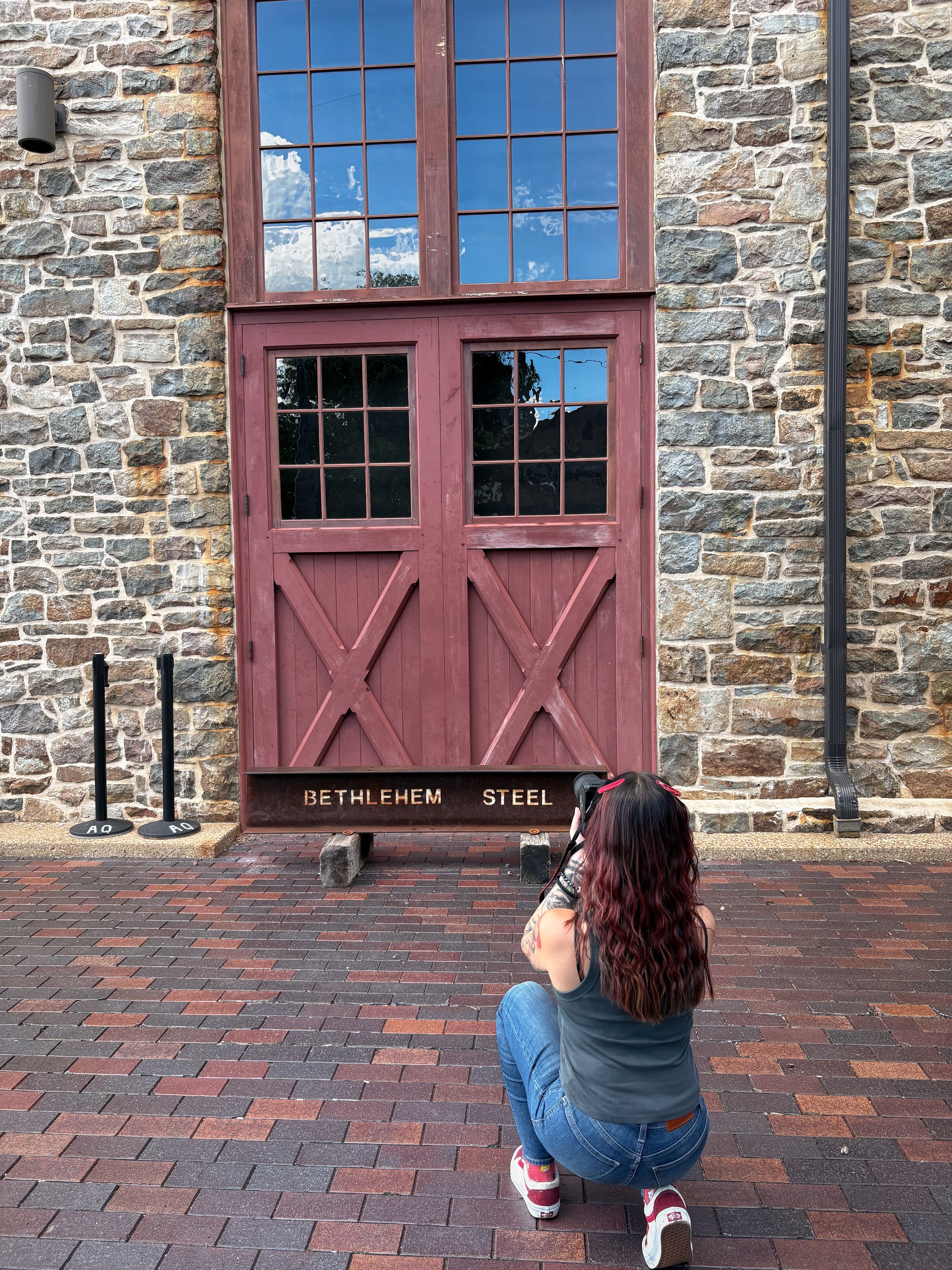Photographer Madison Malik taking a photograph in front of red historic doors and a Bethlehem Steel beam