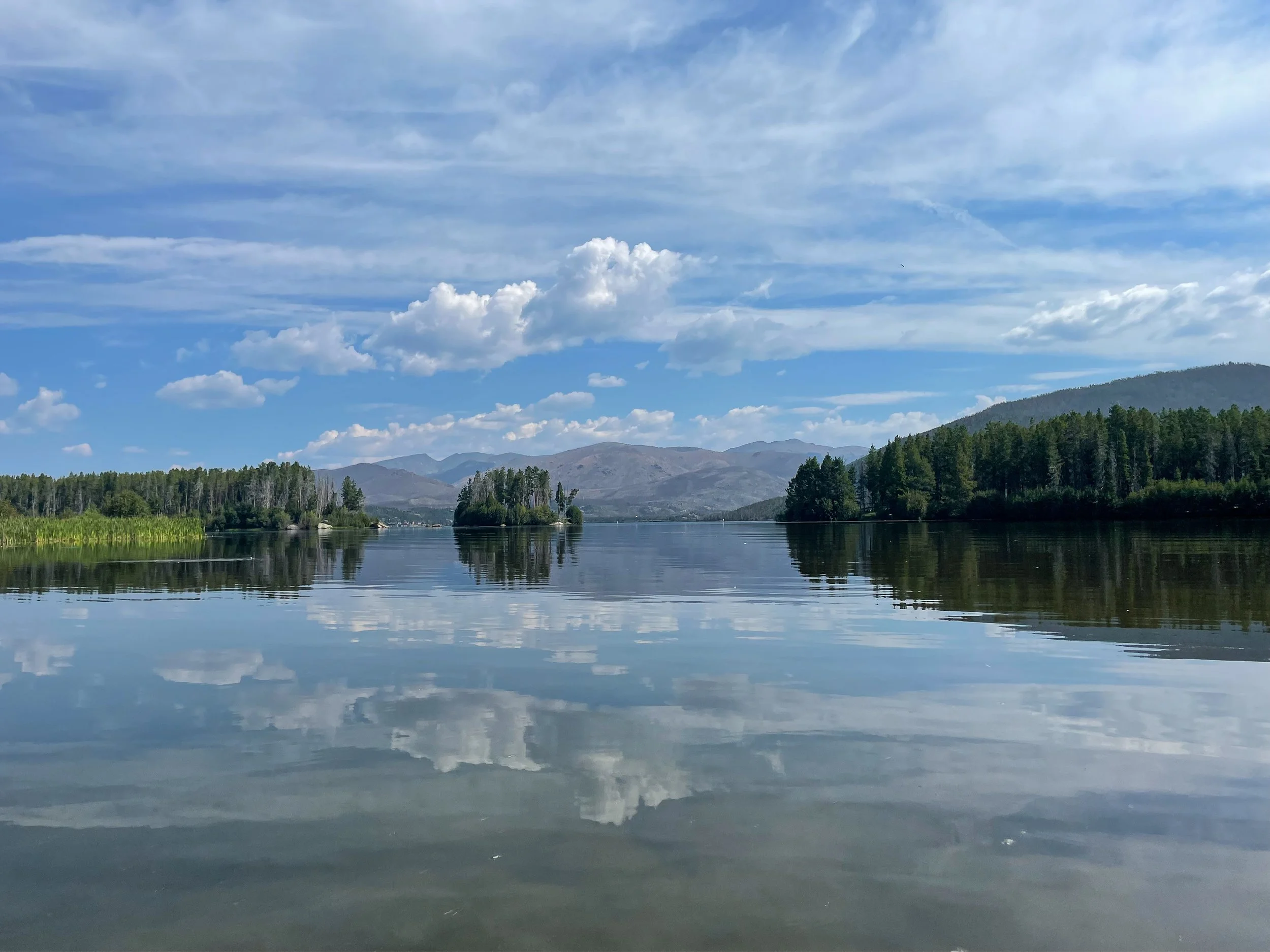 Cloudy skies, rocky mountains, and evergreen trees reflected in the waters of Grand Lake, Colorado