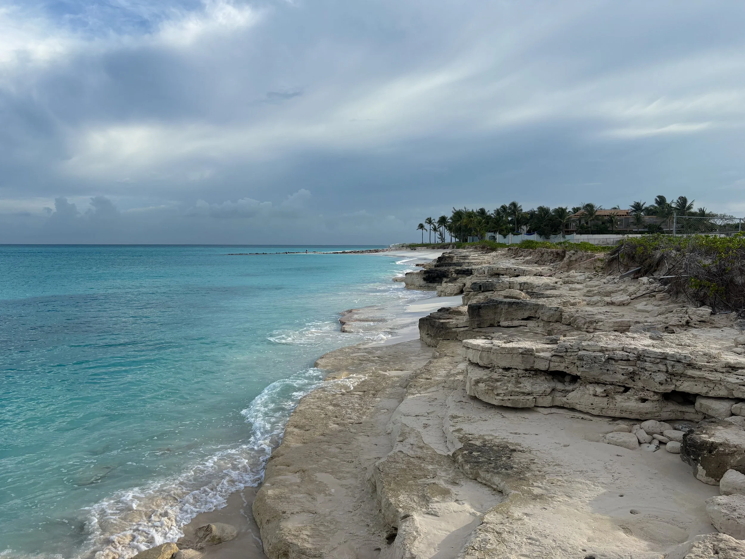 Grace Bay ocean waves meeting natural rock formations with palm trees in the background