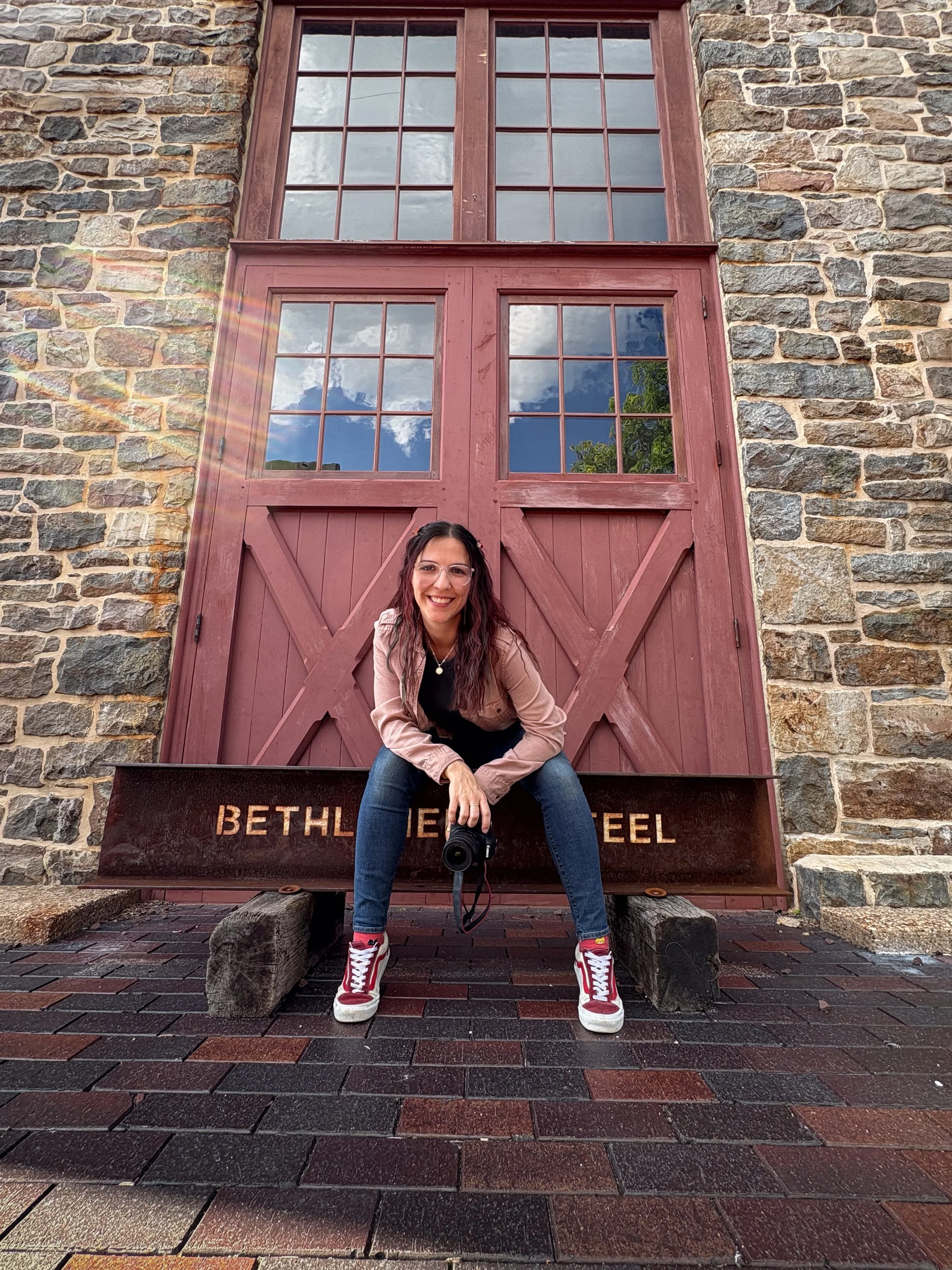 Photographer Madison Malik smiling in front of red historic doors and a Bethlehem Steel beam