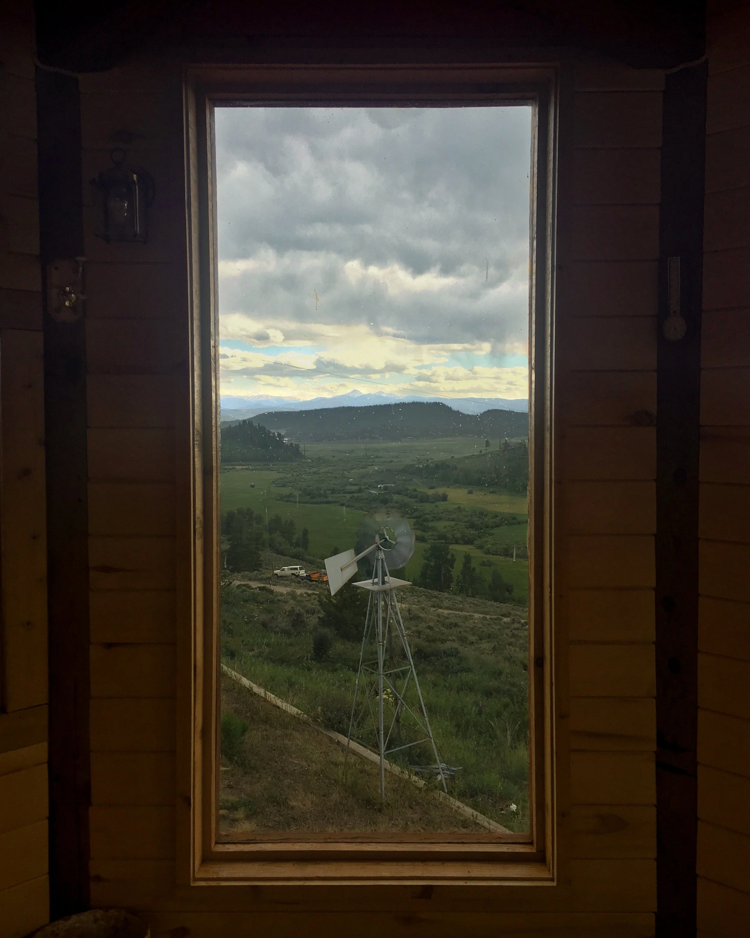 Thunderstorm clouds and rain rolling over rocky mountains, framed by a window from an outdoor patio