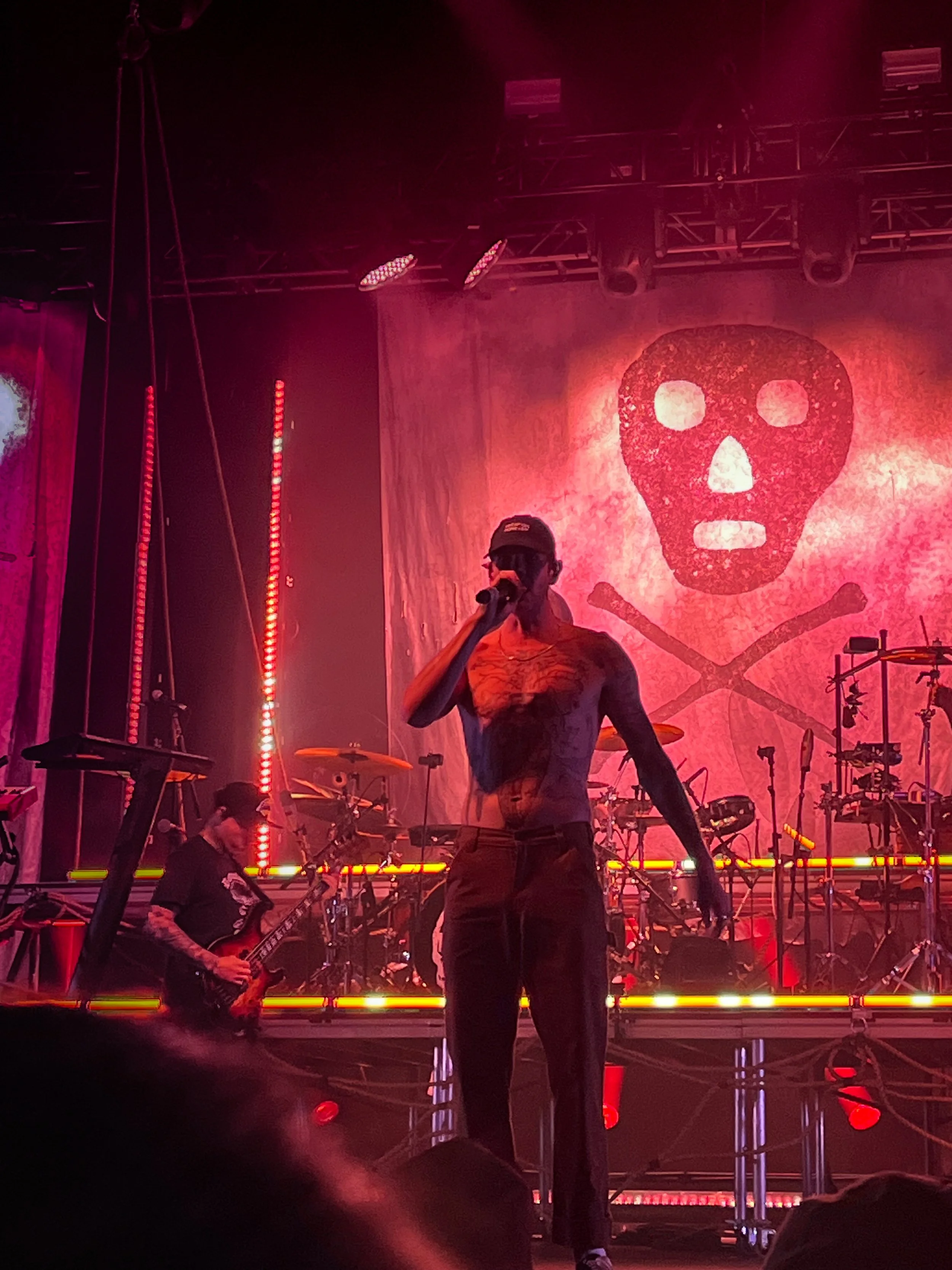 Jared Watson of Dirty Heads singing under red stage lights with a drum set in the background