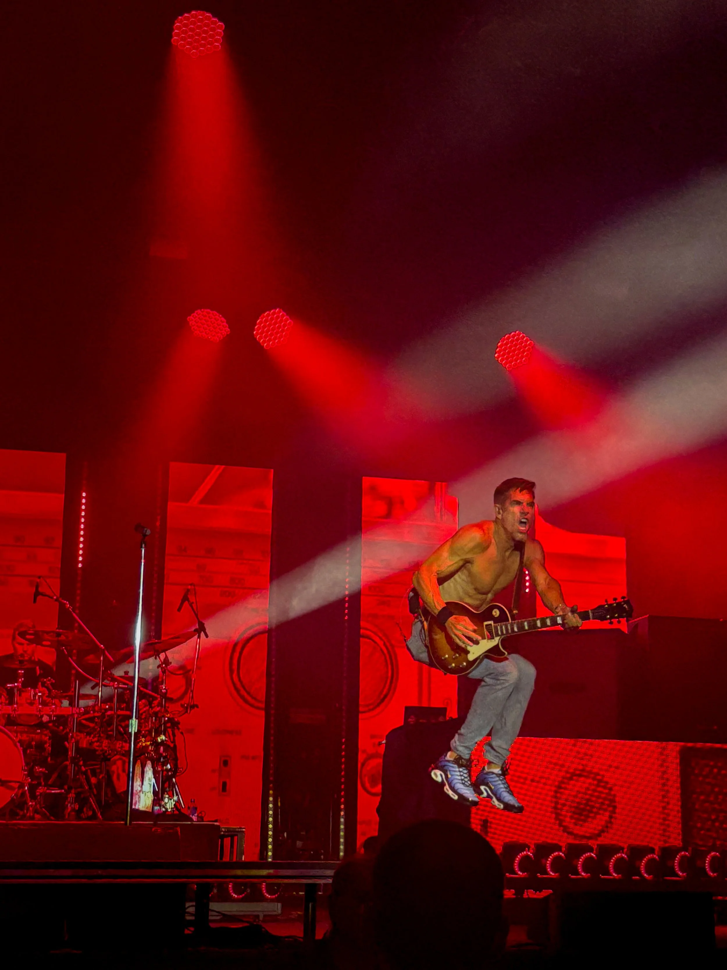 Nick Hexum of 311 jumping while playing guitar under red stage lights