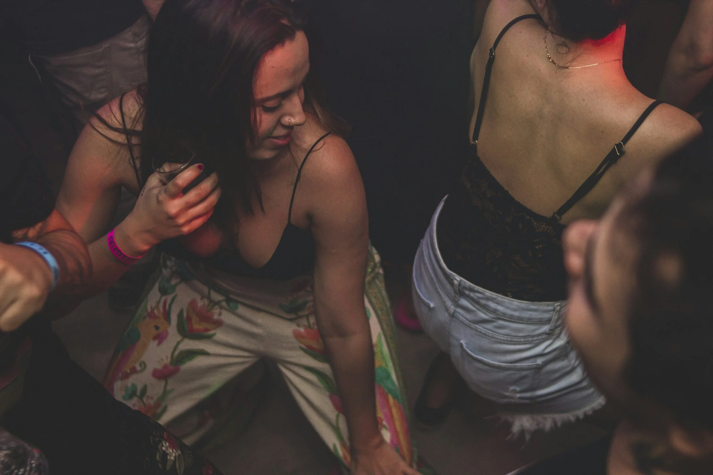 People at a social gathering, some are dancing and holding drinks, with colorful lighting.