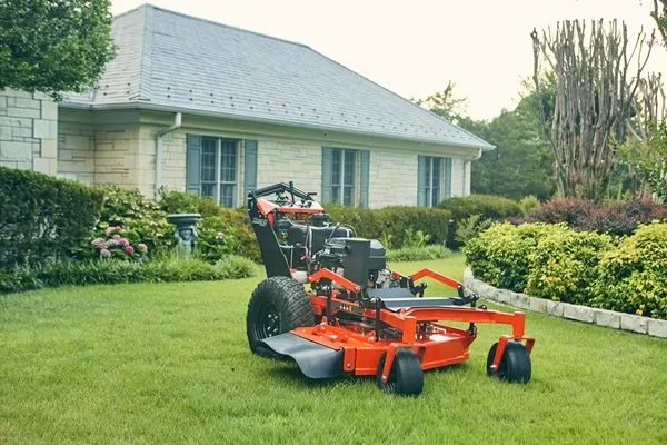 A large red and black riding lawn mower on a well-maintained green lawn in front of a house with a gray roof and beige brick walls.