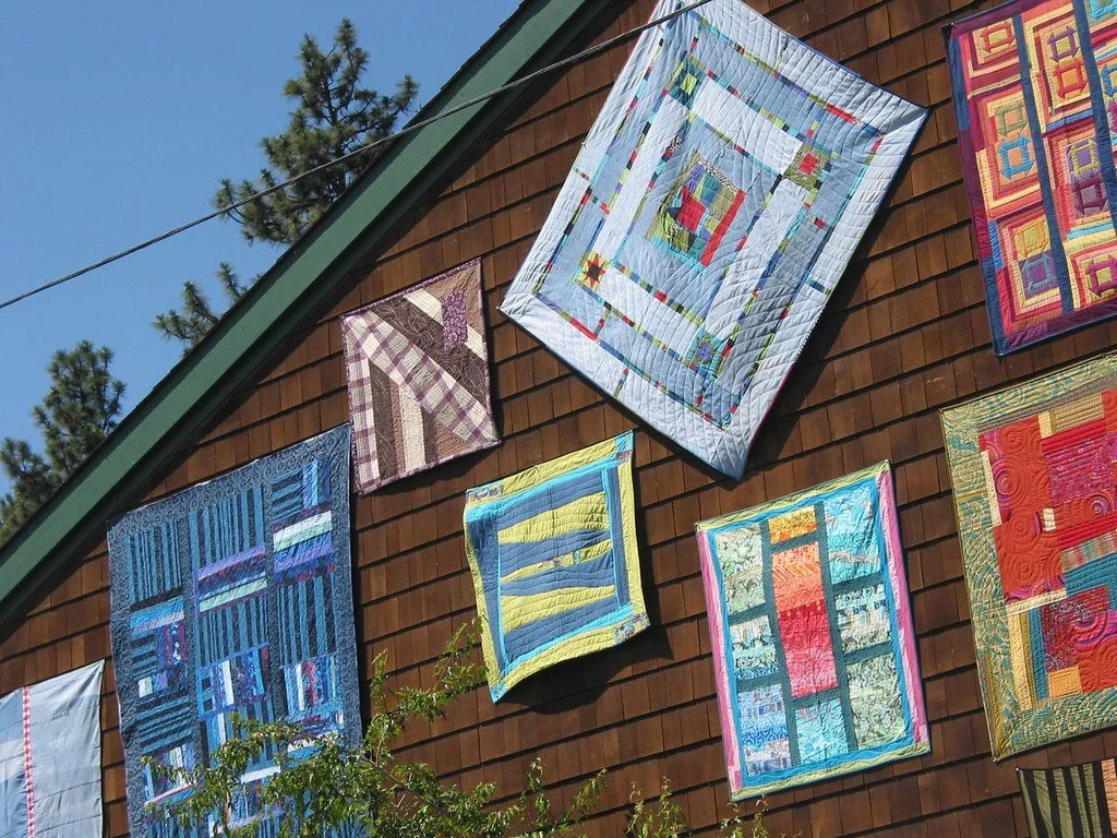 Multiple colorful quilts hanging on an exterior wooden wall at the Sisters Outdoor Quilt Show