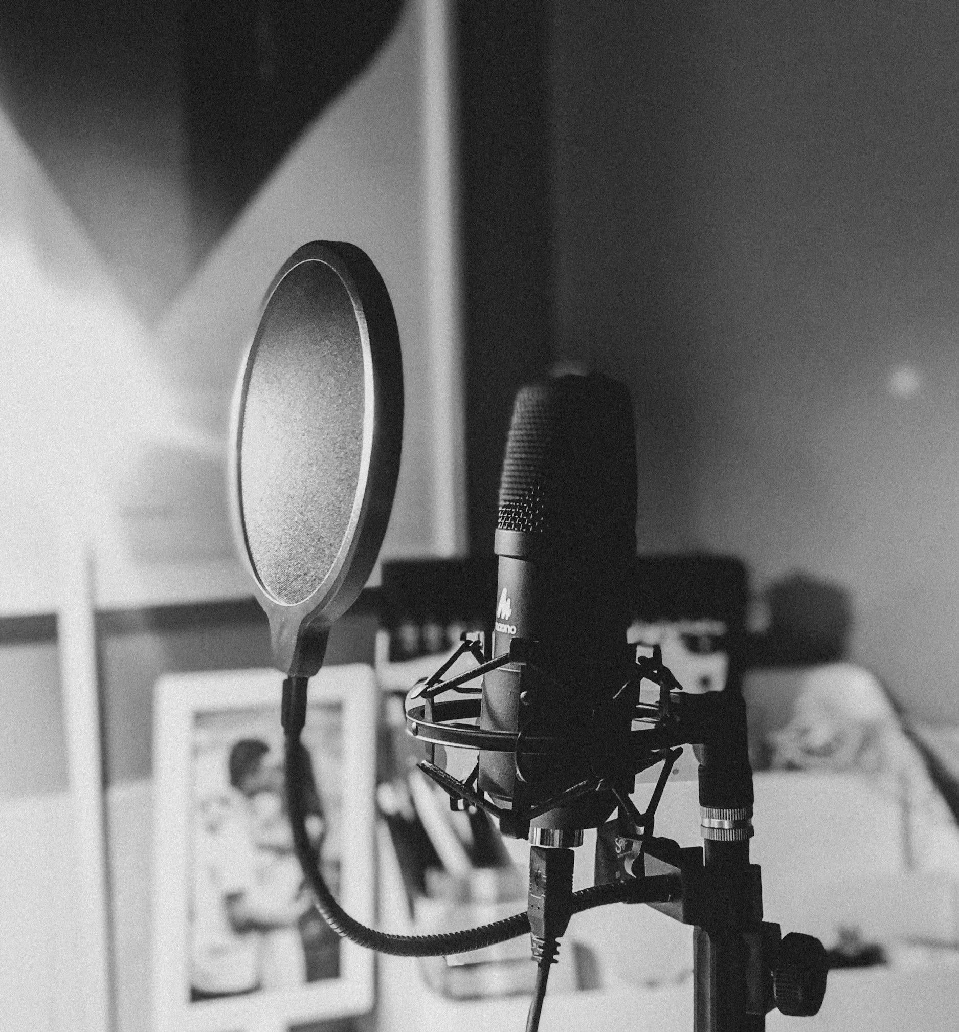 Black and white recording studio with a microphone, pop filter, and soundproofing. In the background, decorated wall and bed with clothes.