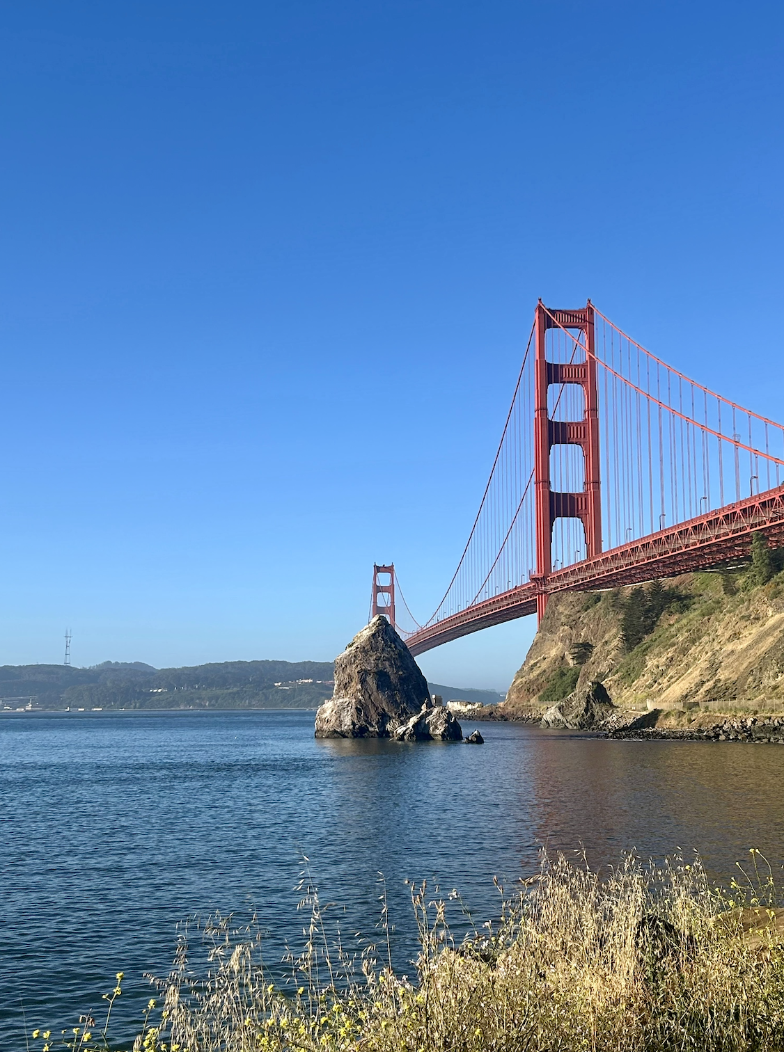 The Golden Gate Bridge in San Francisco, California, with its iconic red towers and suspension cables, spanning across the water with a clear blue sky in the background.