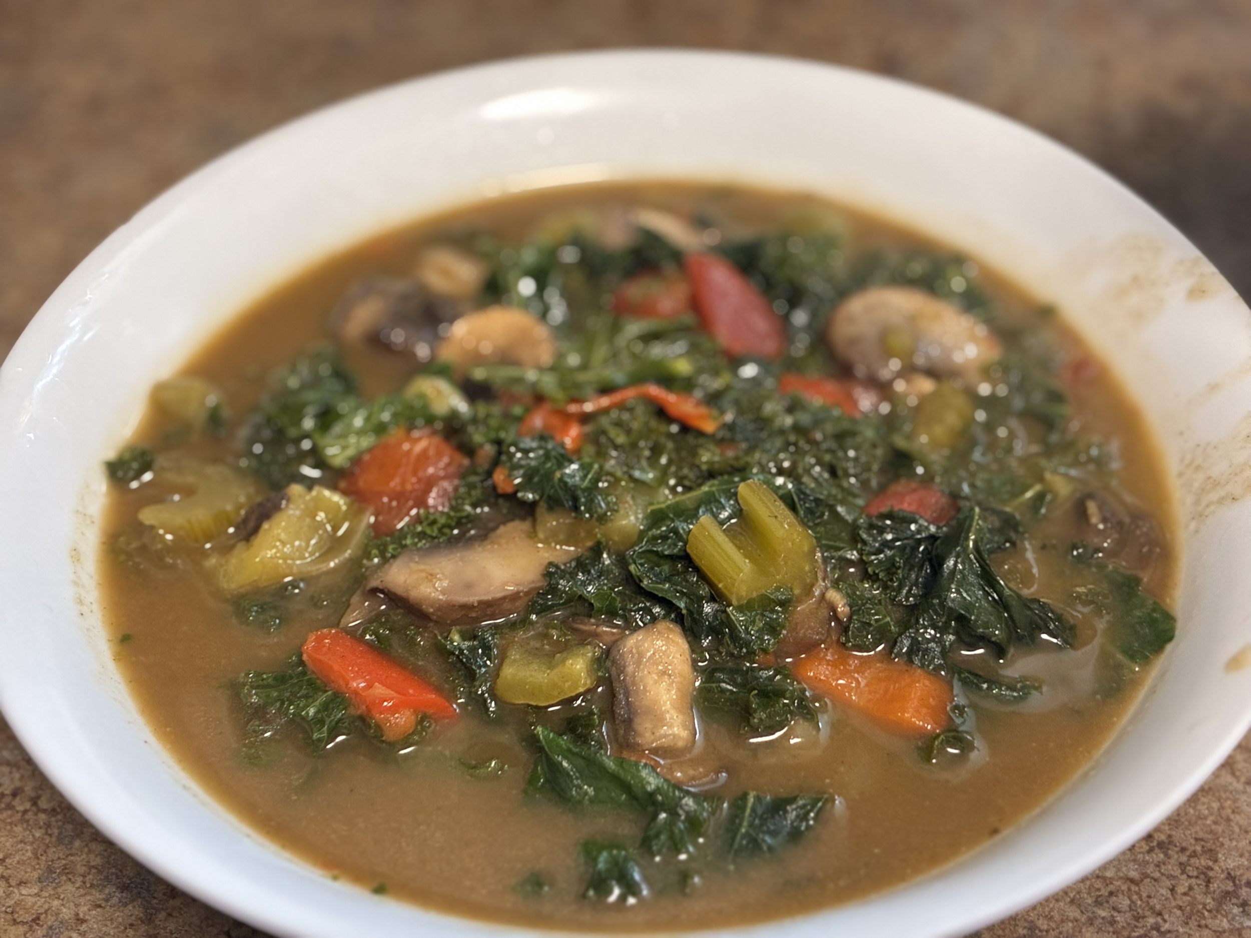 A bowl of vegetable and chicken soup with greens, carrots, celery, and mushrooms.