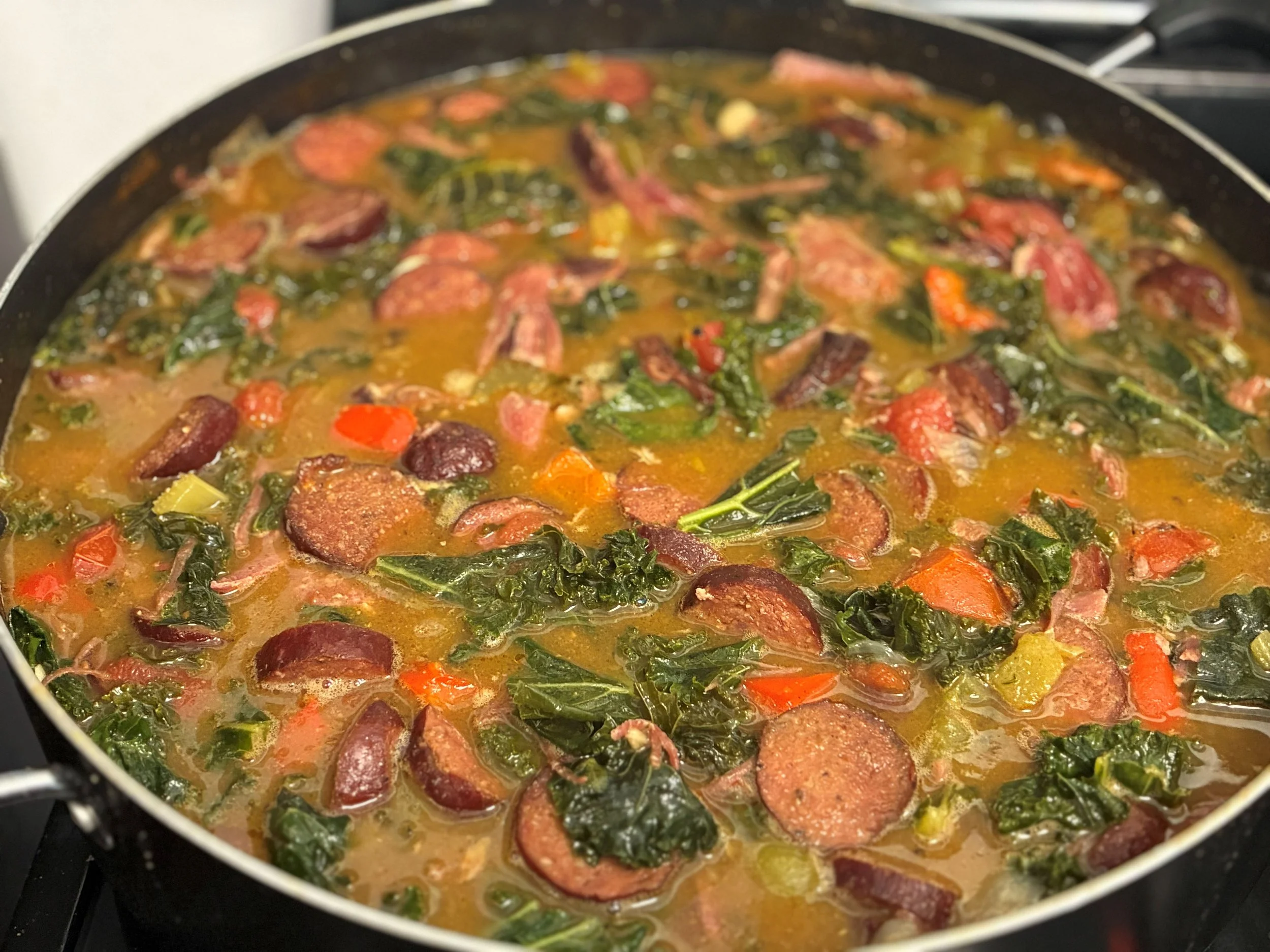 A pot of cooked soup with slices of sausage, chopped spinach, and diced vegetables in broth.