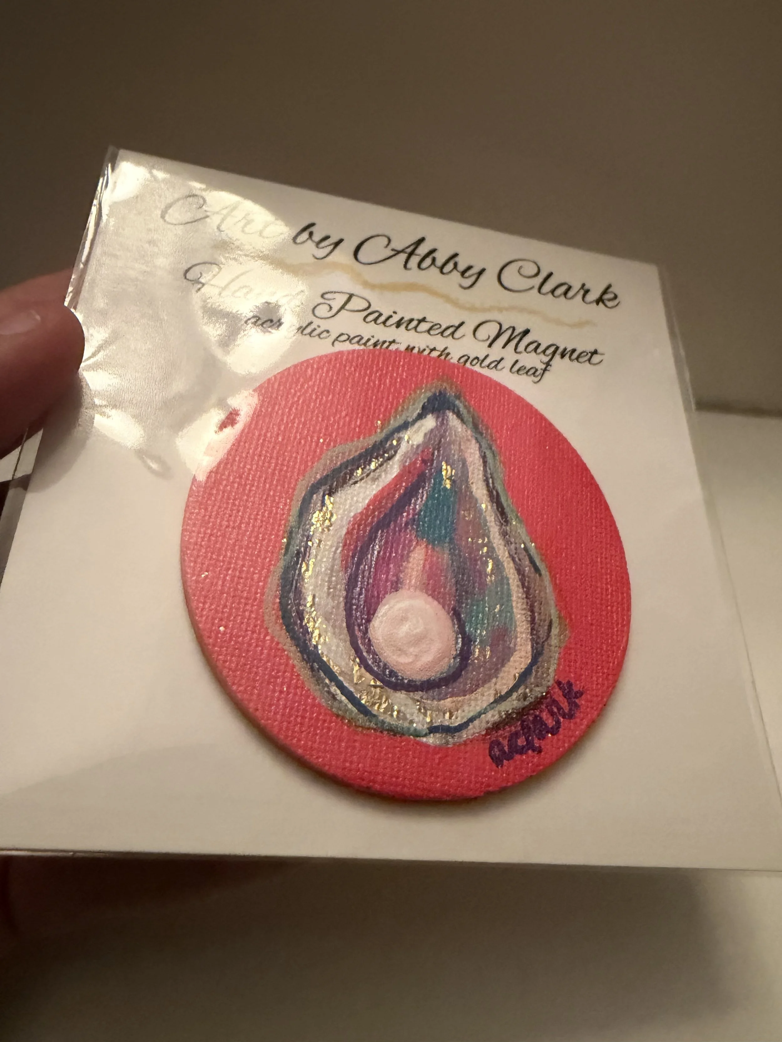 Side view of Abby Clark’s packaged round oyster magnet and its coral-pink painted edge