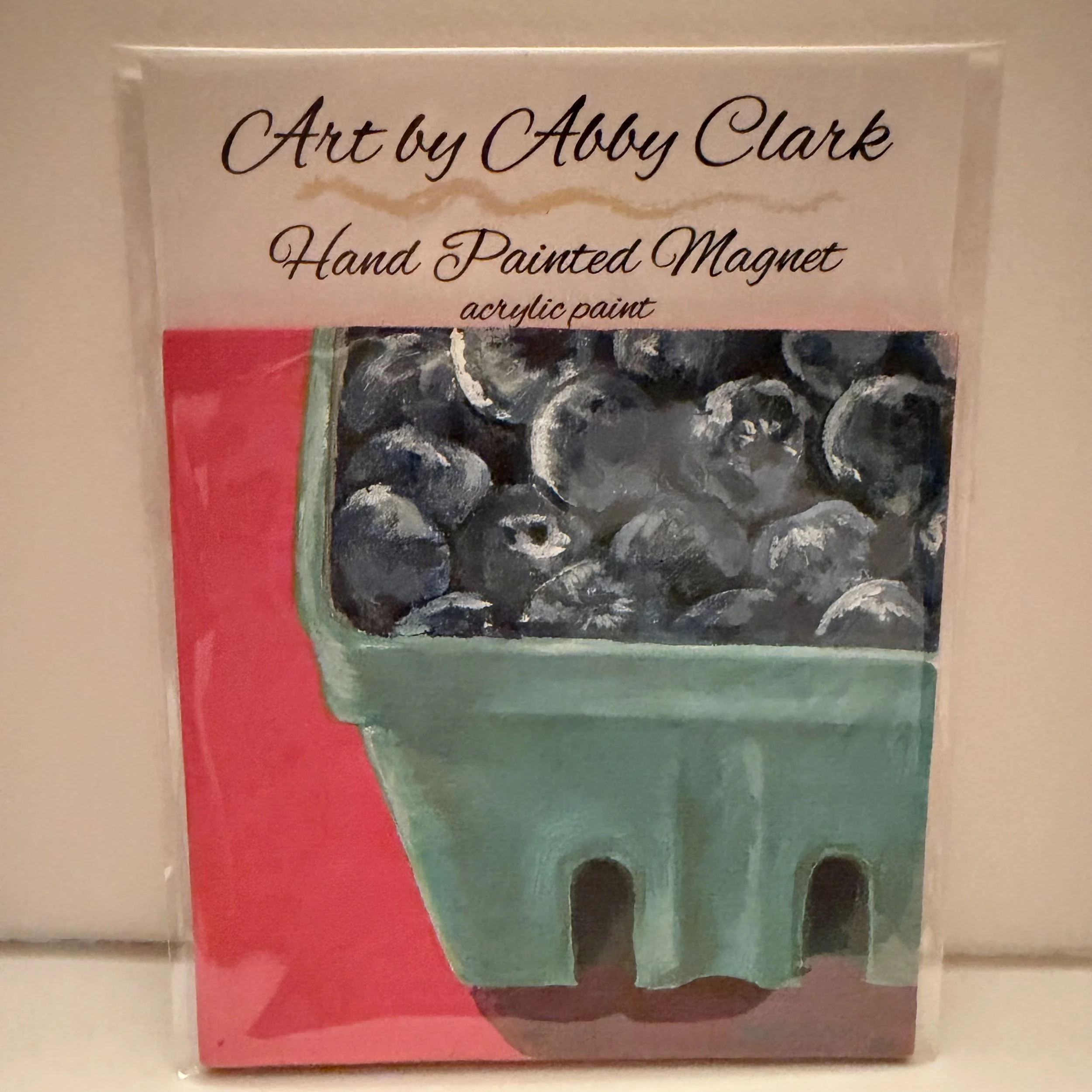 Hand-painted blueberry basket magnet by Abby Clark, with blue berries in a teal basket on coral-pink mini canvas