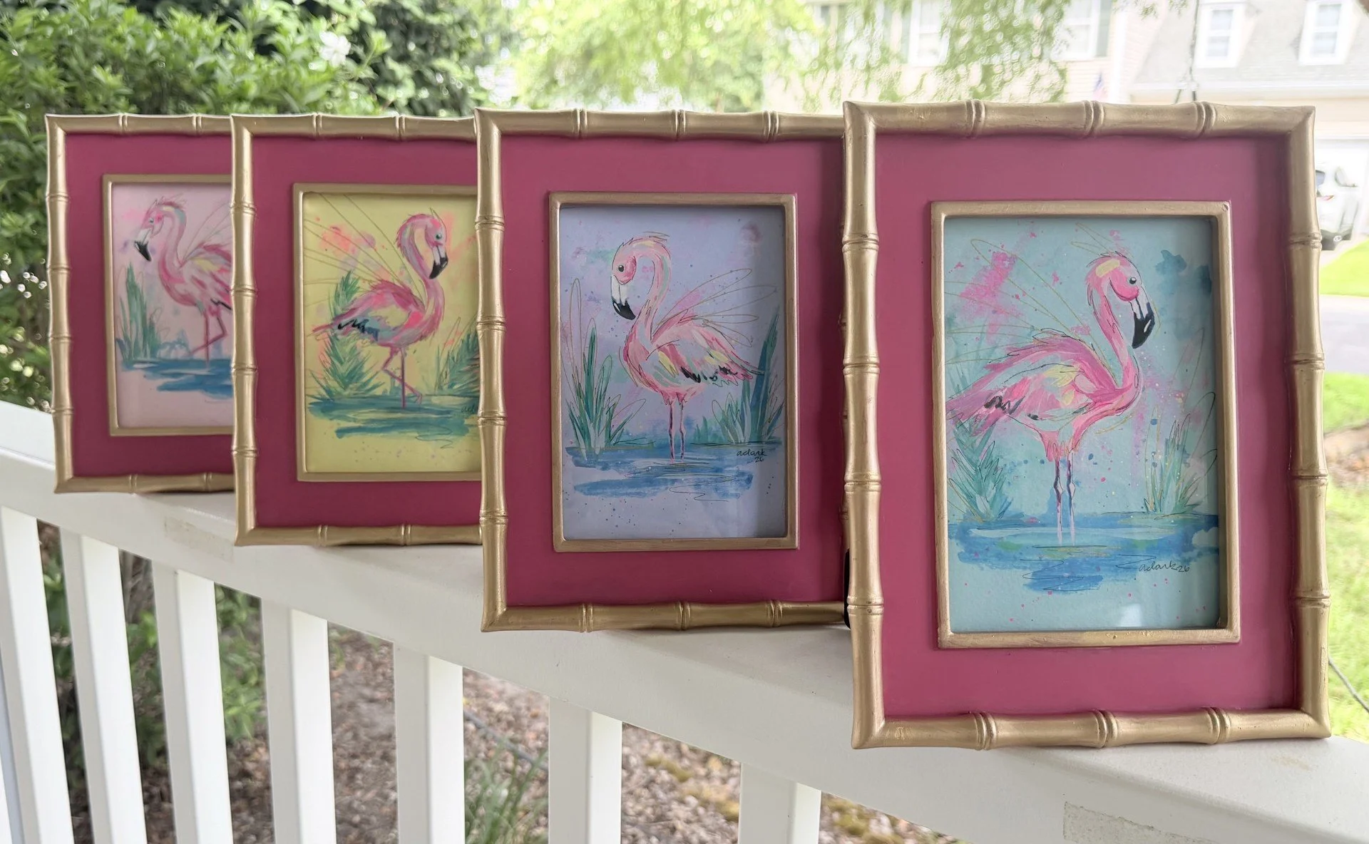 Four colorful flamingo paintings by Abby Clark in gold frames with pink mats