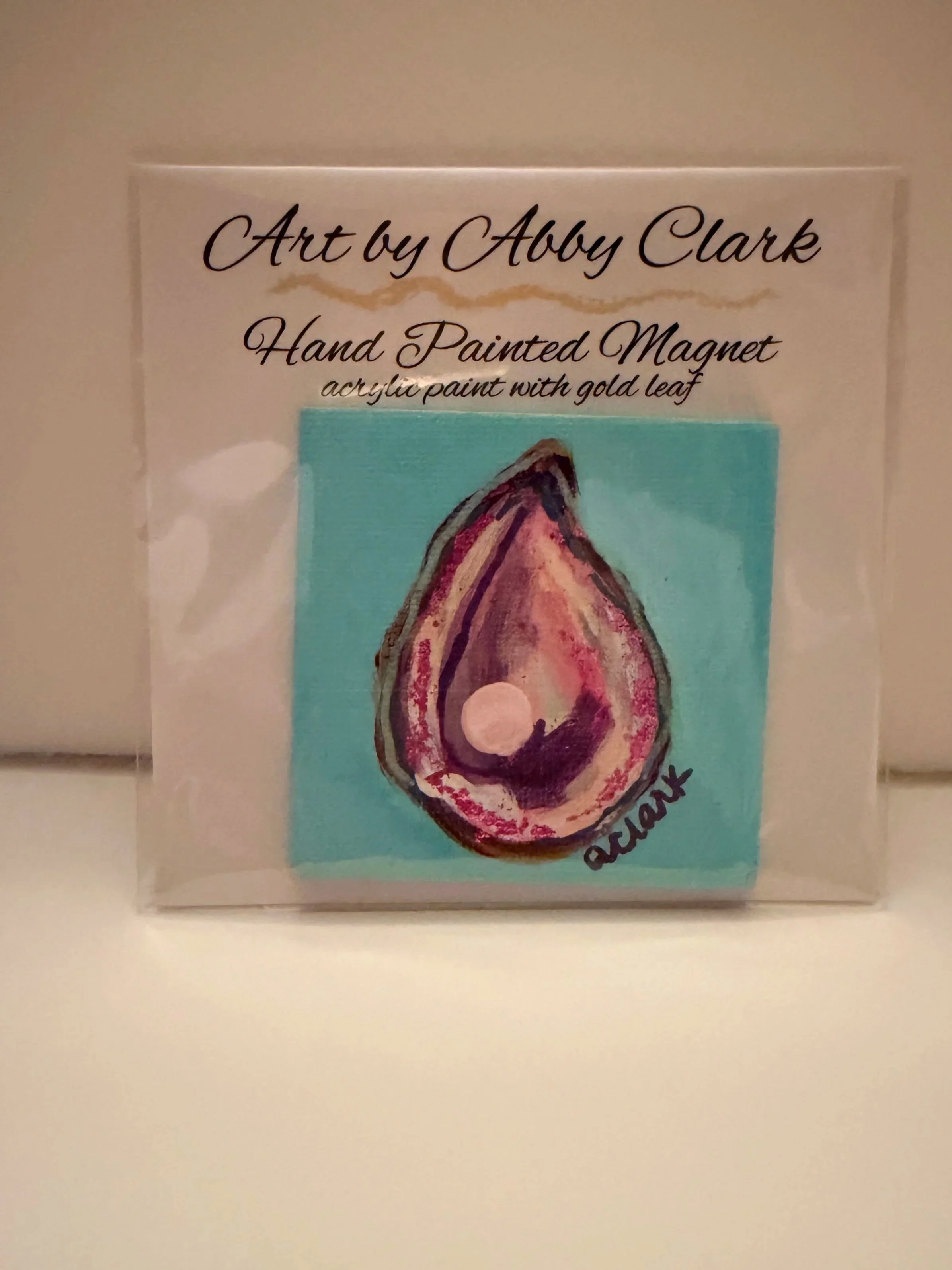 Packaged 2.5 inch square oyster magnet with a raised pearl embellishment against turquoise