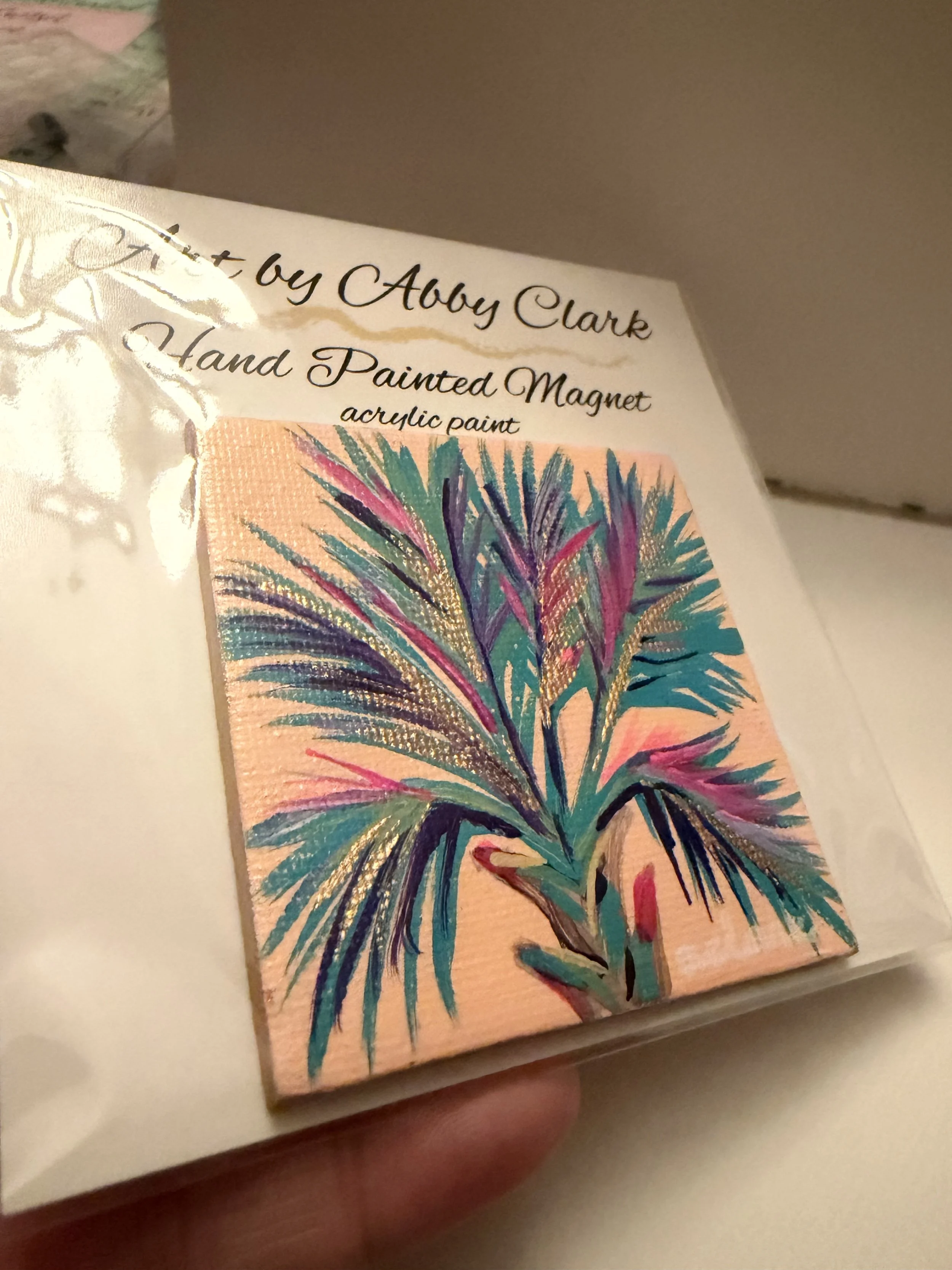 Hand-painted palmetto canvas magnet by Abby Clark with layered colorful fronds against peach