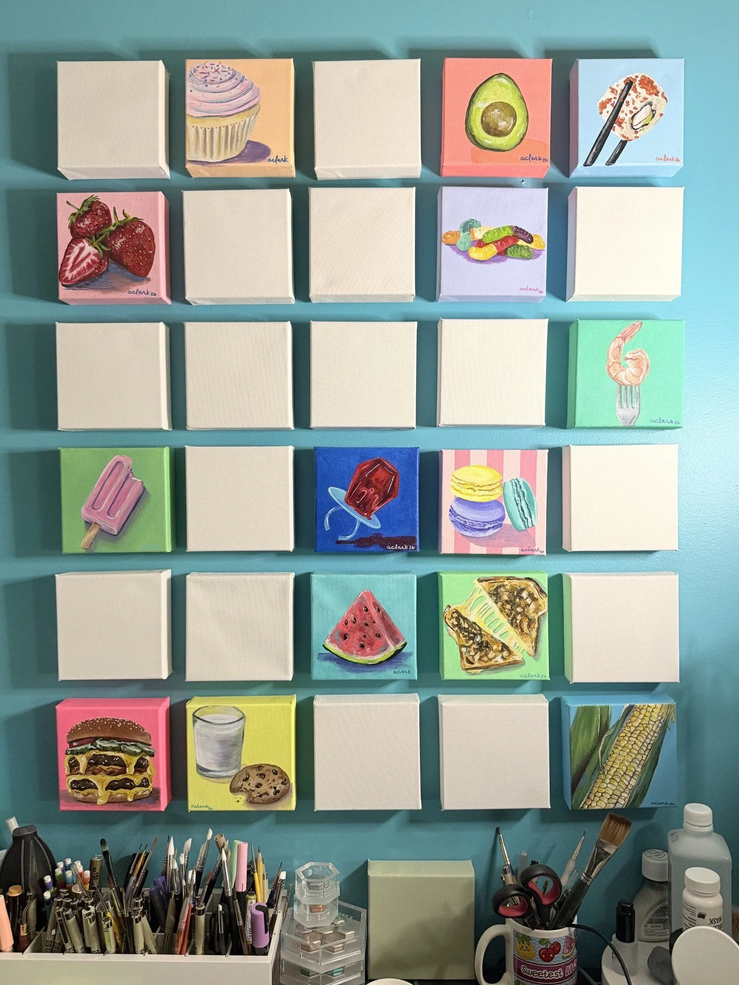 Tastes of Joy paintings in progress, with food paintings and blank canvases arranged on a teal studio wall