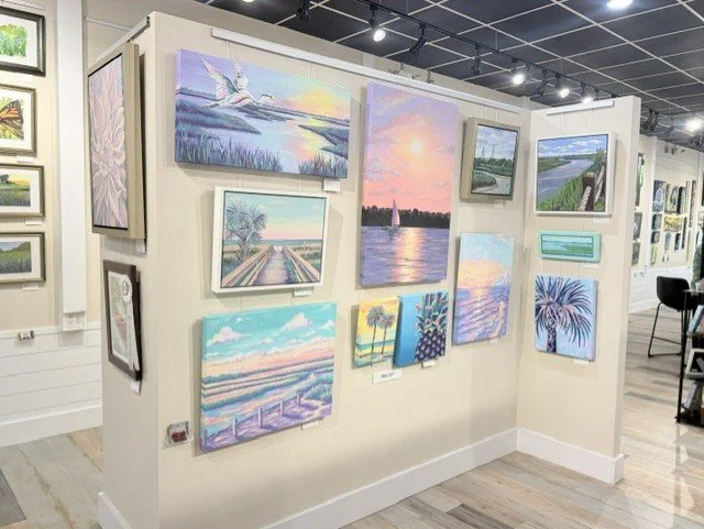 Gallery display of Abby Clark’s colorful Lowcountry paintings, including marshes, palms, and coastal sunsets