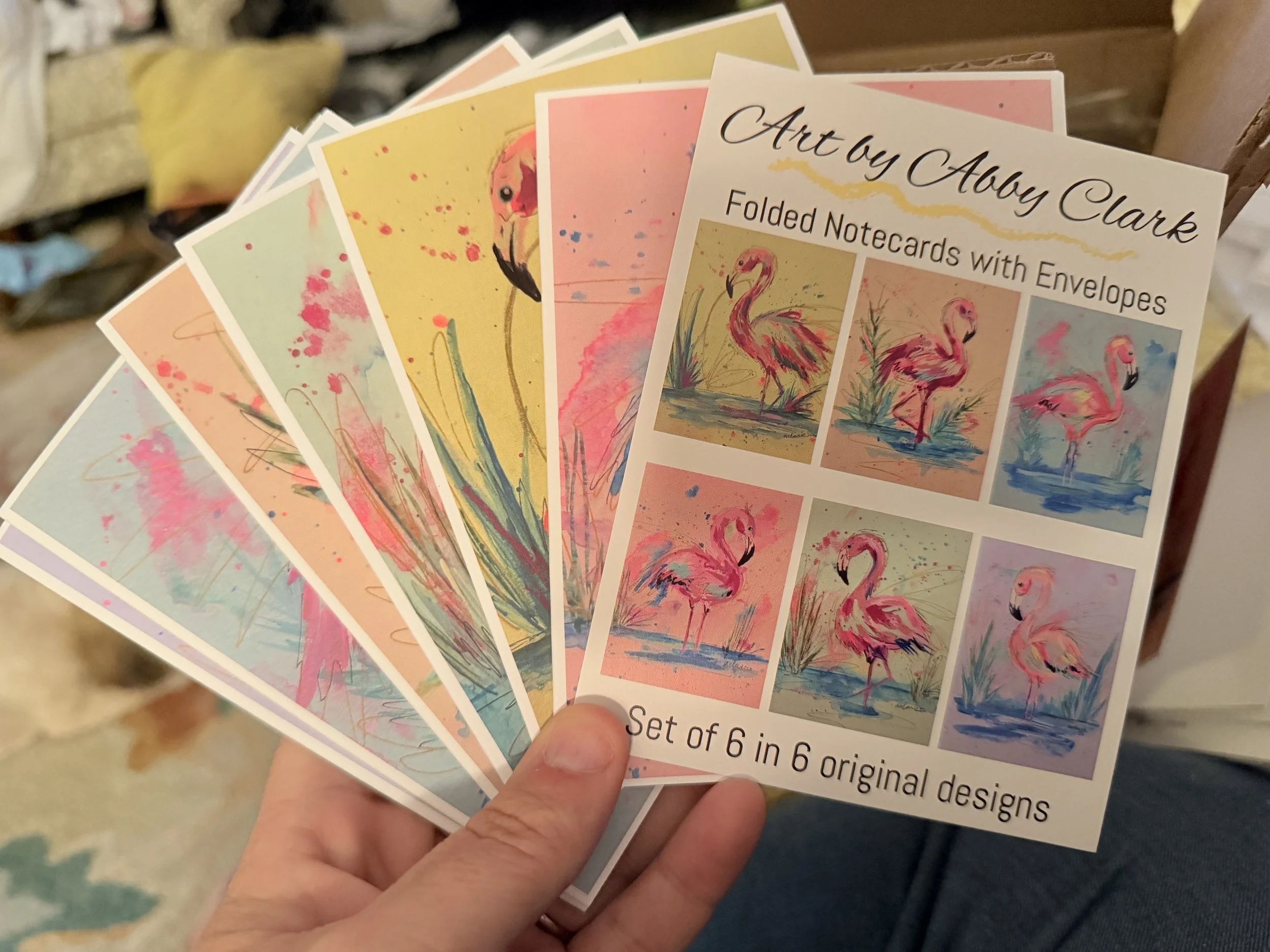 Six packaged flamingo notecards fanned out to show colorful artwork and the set’s cover label