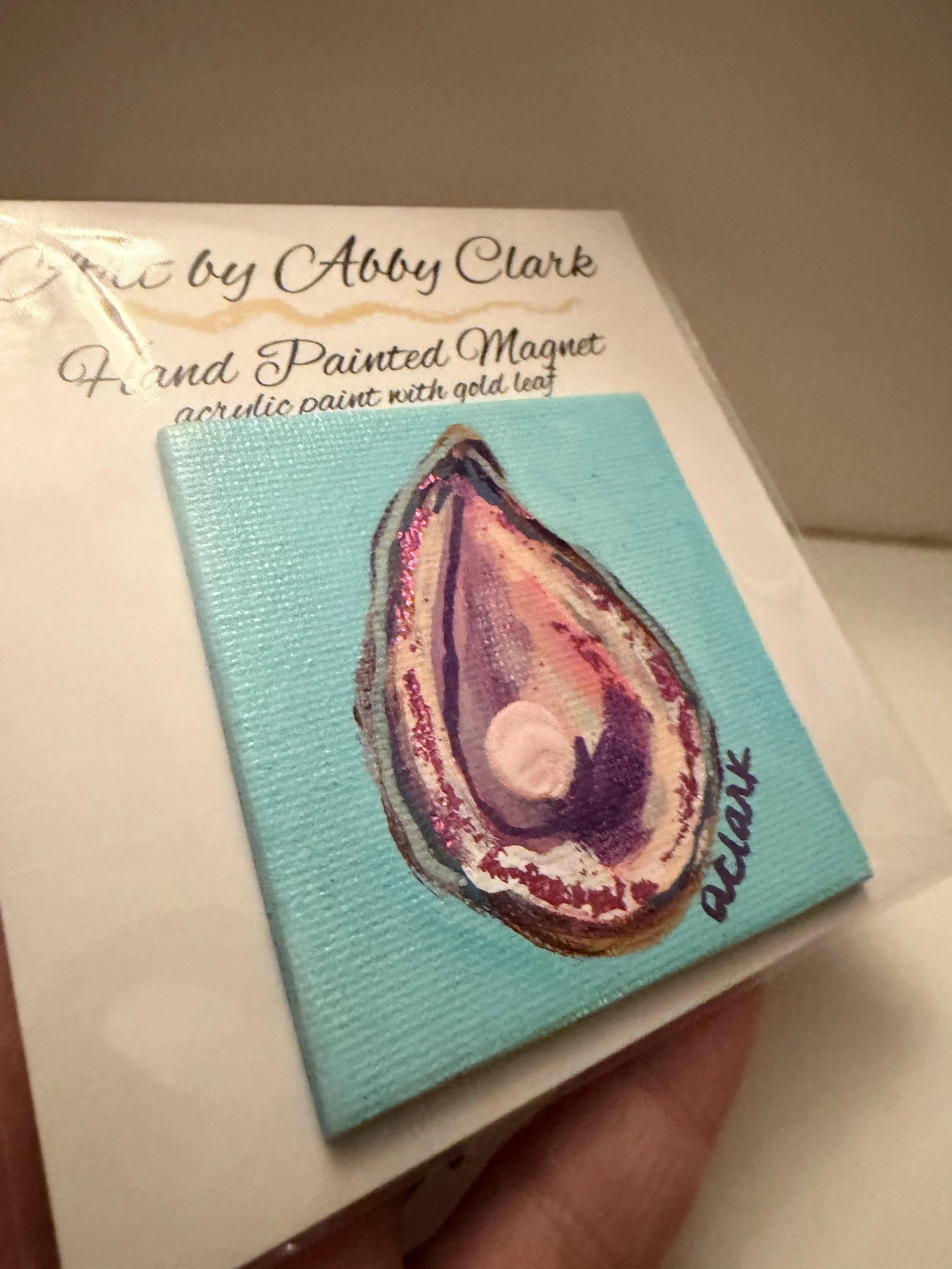 Angled view of the small square oyster magnet, showing its raised pearl embellishment and painted canvas edge