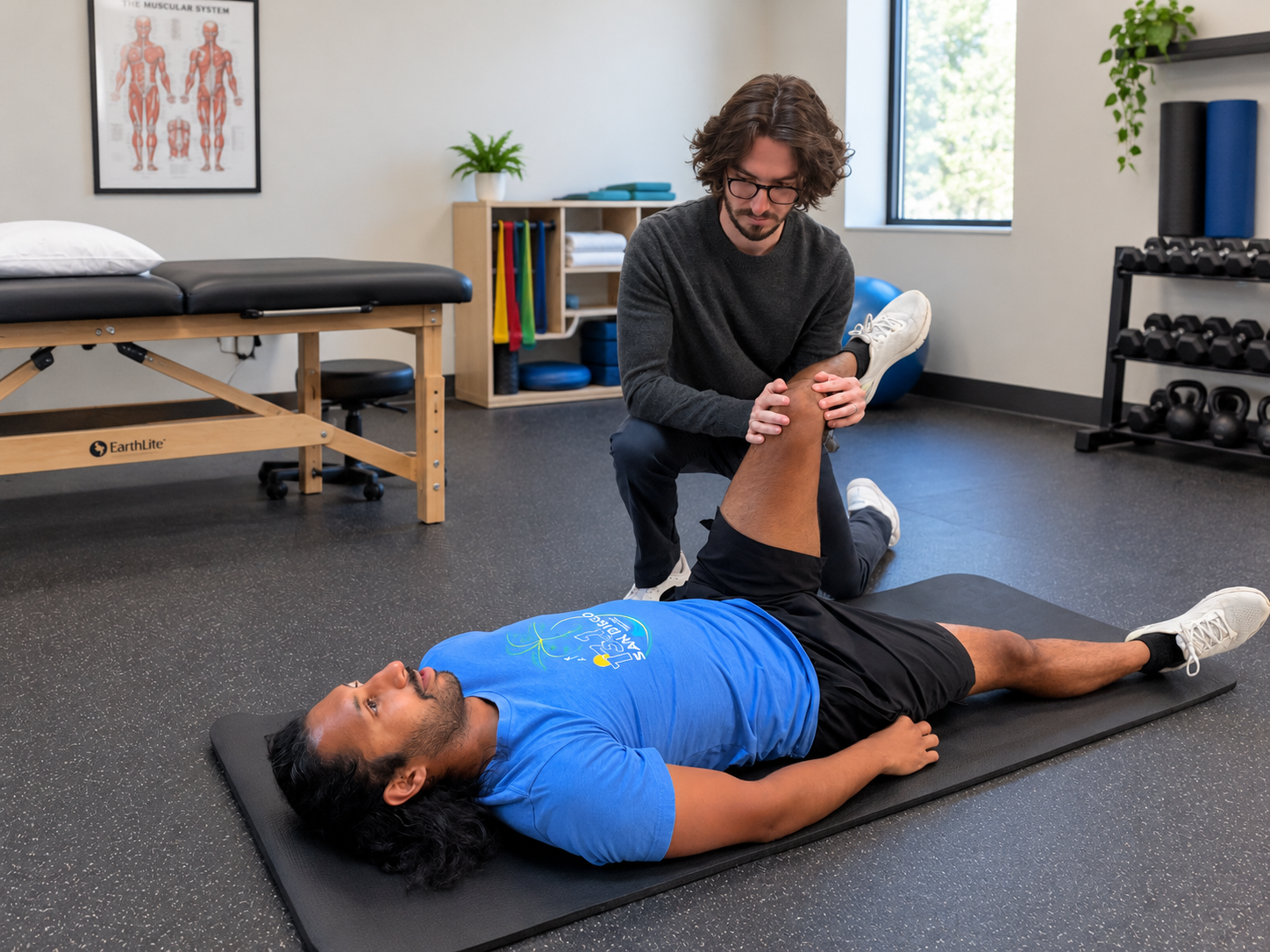 A physical therapist assisting a man with leg stretching exercises on a mat in a therapy room.