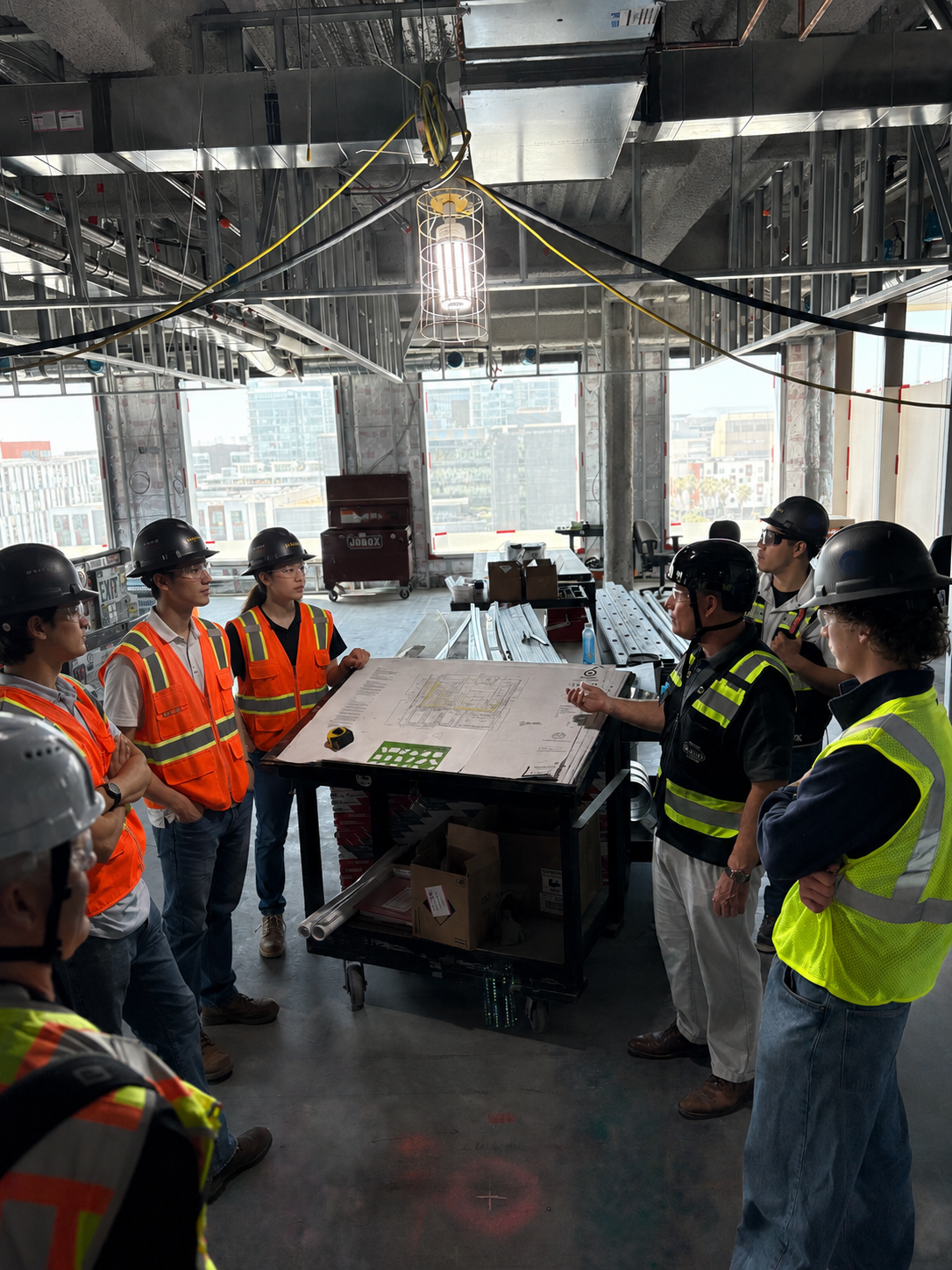 AR&B CEO, Rich Buckley, with mechanical construction workers and engineers gathered around a table with blueprints and plans, discussing at a high-rise building site.