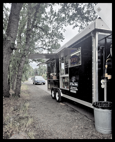 Food truck parked on a grassy area with an open service window and an 'OPEN' sign, surrounded by trees.
