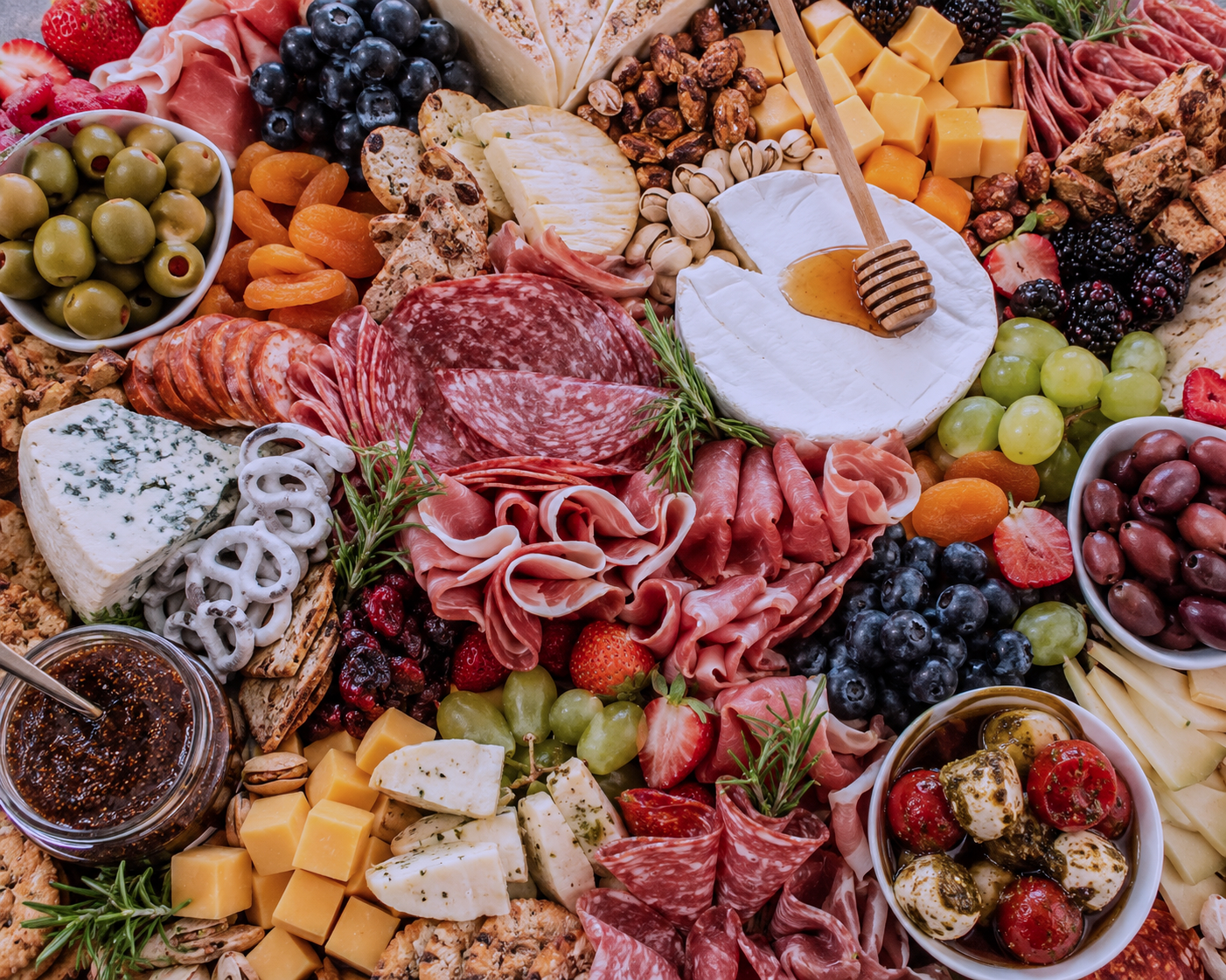 An assortment of cheeses, cured meats, fresh fruits, nuts, and condiments on a charcuterie board.