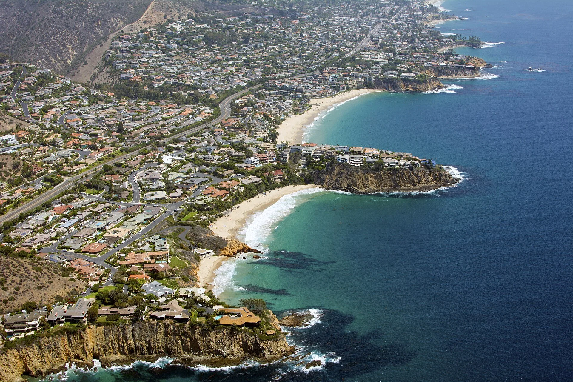 Aerial view of a coastal town with houses on cliffs, a sandy beach, and the ocean.