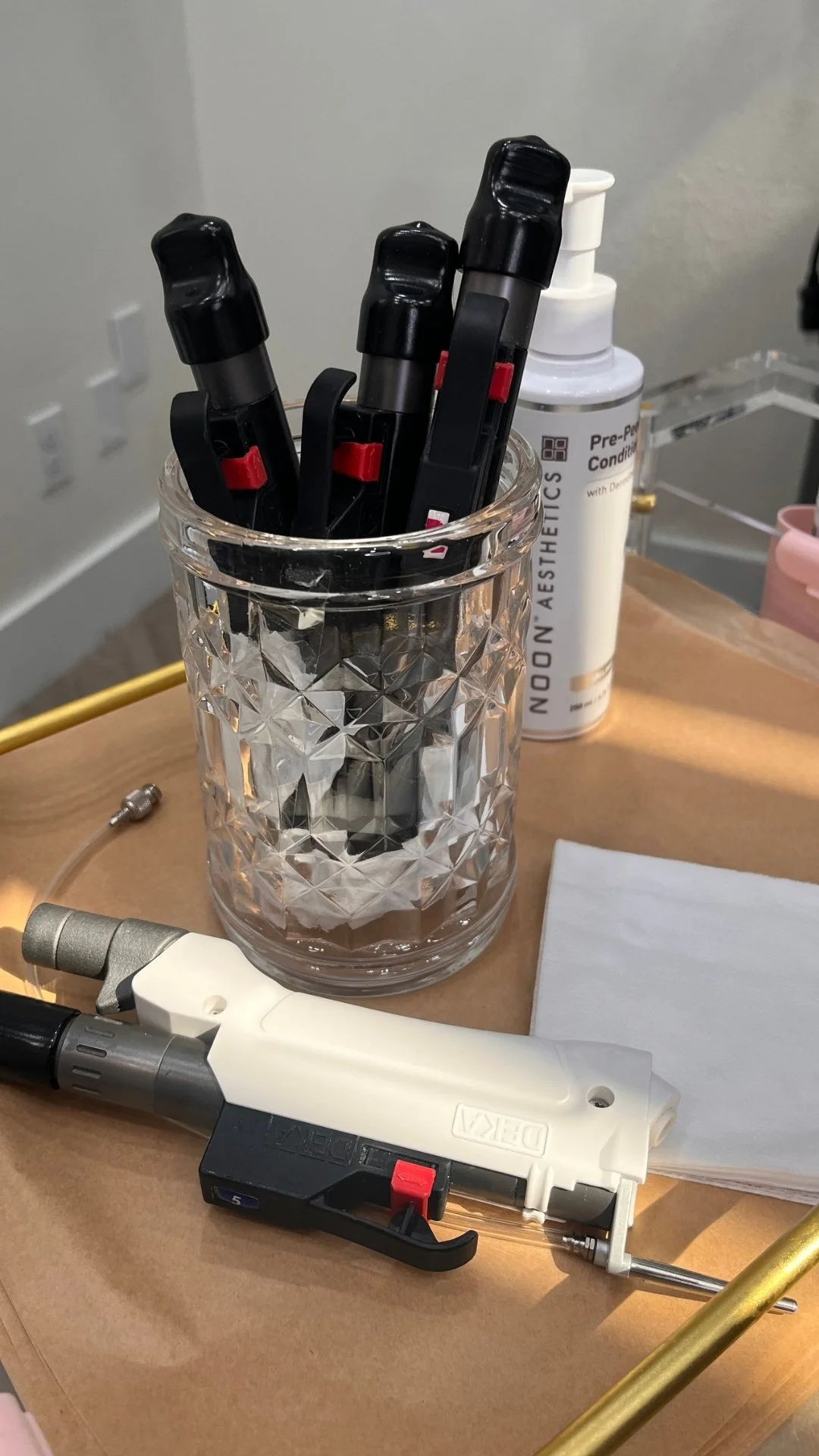 The Moveo laser handpieces are placed inside textured glass container, a white container of pre-procedure conditioning spray, and a white napkin, on a treatment table.
