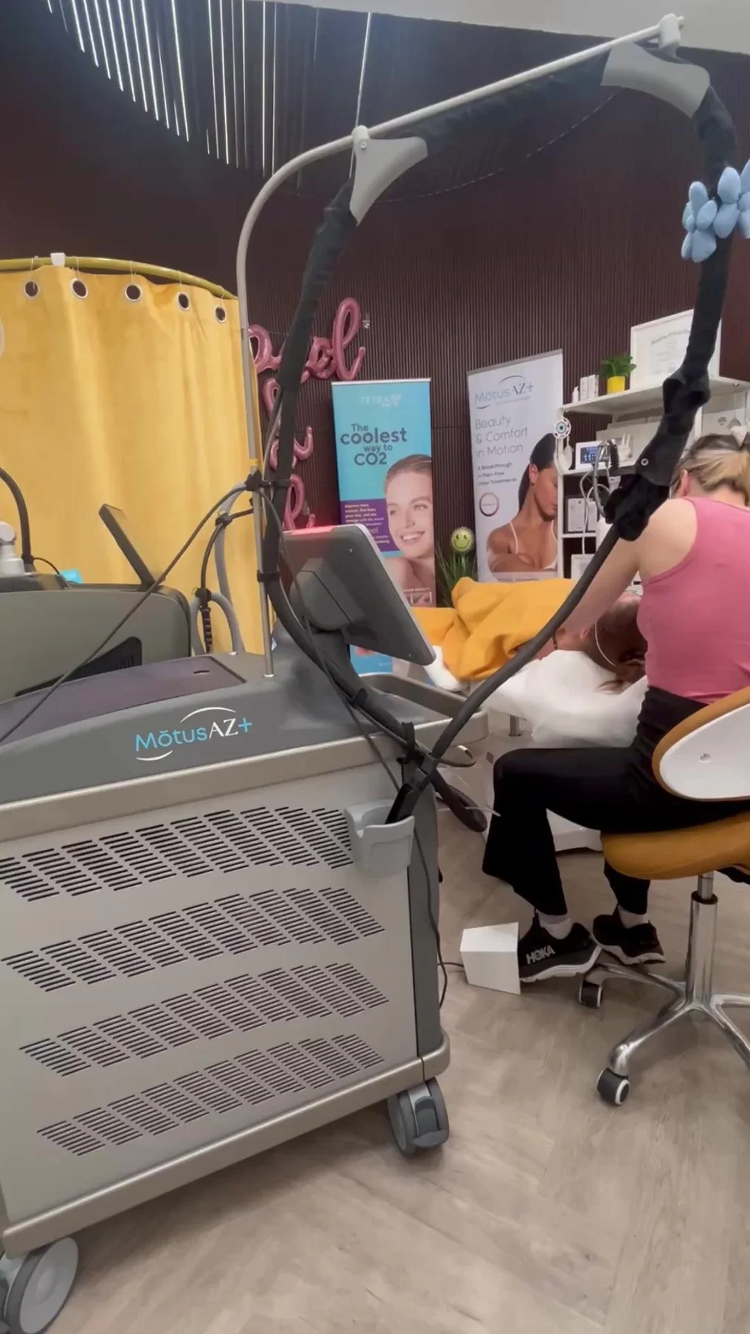 A person receiving a Moveo VL treatment while lying on a treatment bed, with a medical device labeled 'MOTUS AZ+' nearby, in a medical spa setting.