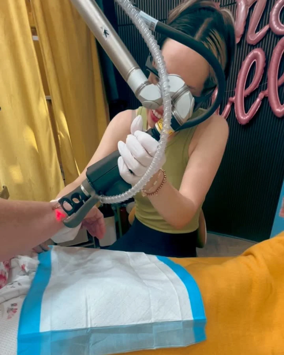 A woman smiling and holding the Tetra Pro CO2 device, performing a CoolPeel CO2 treatment on a hand.